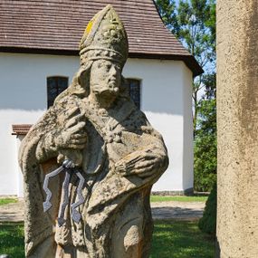 Zdjęcie nr 1: Kapliczka ustawiona na niskim prostopadłościennym postumencie. Pośrodku na wysokim cokole umieszczona kolumna, na której szczycie ustawiona jest figura Matki Boskiej Niepokalanie Poczętej z Dzieciątkiem. Cokół flankowany szerokimi spływami wolutowymi, na których ustawione są na niskich podstawach rzeźby: po lewej św. Donata, a po prawej św. Floriana. Na przedniej ściance cokołu znajduje się płaskorzeźba św. Marii Magdaleny ujęta płyciną w kształcie stojącego prostokąta, zamkniętego łukiem nadwieszonym z uskokami. Święta ukazana jest na tle groty, zwrócona trzy czwarte w prawo z rozpuszczonymi włosami, z dyscypliną w dłoni. Po lewej stronie kompozycji znajduje się wysoki, prosty krzyż i czaszka. Nad płyciną napis „ANNO D(OMI)NI 1758 / S(ANCTA) MARIA MAGDALENA / Zda SPPIPM”. Na tylnej ściance cokołu rzeźba św. Rozalii, ukazana w podobnym ujęciu z napisem „SANCTA ROSALIA VIRGO”. Święty Donat ukazany w postawie stojącej w delikatnym kontrapoście z księgą w lewej dłoni i trójzębem w prawej. Ubrany jest w strój biskupi: albę, komżę, kapę, infułę, rękawice i buty. Ma szeroką twarz, okoloną krótką brodą, bujne i długie włosy spływające na plecy. Na podstawie napis: „S(ANCTUS) DONATUS”. Po prawej stronie kolumny rzeźba św. Floriana, ustawionego frontalnie, który prawą ręką polewa wodą płonący dom, a lewą podtrzymuje u ramienia połę płaszcza. Ubrany jest w strój legionisty rzymskiego z hełmem o wyraźnie podkreślonym pióropuszu. Twarz szeroka, okolona średniej długości włosami, schowanymi pod hełmem. Podstawa pod rzeźbą opleciona metalowymi ściskami. Kolumna ustawiona na bazie, trzon gładki, dekorowany w połowie wysokości dwiema uskrzydlonymi główkami aniołów na tle promienistej glorii, kapitel koryncki. Rzeźba Matki Boskiej Niepokalanej z Dzieciątkiem na prawym ręku ustawiona jest frontalnie, w delikatnym kontrapoście na globie ziemskim, oplecionym przez węża. Maria ubrana jest w długą suknię i silnie drapowany płaszcz. Twarz owalna, okolona bujnymi i długimi włosami. Dzieciątko zwrócone jest w stronę Matki Boskiej. Rzeźba Marii osłonięta jest metalowym daszkiem wspartym na czterech prętach przytwierdzonych do metalowej opaski oplatającej kapitel kolumny. Kapliczka obwiedziona metalowym płotkiem. 

