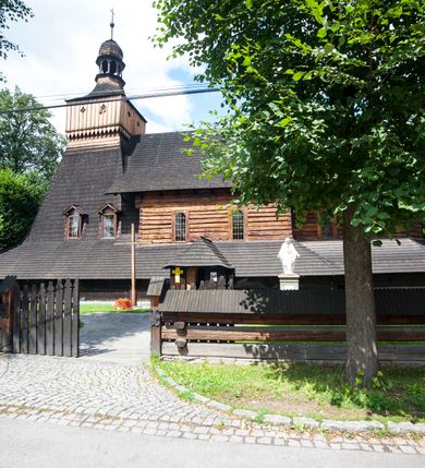 Zdjęcie nr 26: Drewniany kościół pw. św. Marcina w Jawiszowicach jest budowlą orientowaną, wzniesioną na zrąb. Do węższego prezbiterium zamkniętego trójbocznie przylega szersza nawa na rzucie zbliżonym do kwadratu. Od północy przy prezbiterium wybudowano zakrystię na planie wydłużonego prostokąta, a od zachodu wieżę w konstrukcji na słup na rzucie kwadratu. Zwieńczono ją izbicą z baniastym hełmem z latarnią. W przyziemiu wieży urządzono kruchtę. Nawę z prezbiterium nakryto jednokalenicowym dachem z więźbą w układzie storczykowym z przypustnicami (nadbitkami). W węższej części prezbiterialnej dach wsparty jest na trójkątnych zastrzałach widocznych na zewnątrz. Nad prezbiterium wznosi się sygnaturka w formie latarni z baniastym hełmem zwieńczonym krzyżem. Bryłę kościoła w całości otaczają arkadowe soboty z drewnianymi parapetami i z prześwitami wypełnionymi półprzeźroczystą pleksą. Na wysokości wejścia południowego do kościoła linię sobót wysunięto do przodu, dzięki czemu powstała pseudokruchta nakryta dachem siodłowym. Zarówno dach kościoła, jak i zakrystii, sobót oraz hełmy wieży i sygnaturki pokryte są gontem. Ściany nawy i prezbiterium utworzone z poziomo układanych bali przepruwają prostokątne okna z wpisanym łukiem półokrągłym, stanowiącym część stolarki okiennej. Na osi prezbiterium za ołtarzem głównym wycięto okulus. Wnętrze kościoła w nawie nakrywa płaski strop ze skośnym szalowaniem po bokach, a w prezbiterium pozorne sklepienie kolebkowe. Prezbiterium od nawy oddziela półokrągła tęcza z profilowaną belką, na której umieszczono grupę Ukrzyżowania. Całość wnętrza zdobi wielobarwna, ornamentalno-figuralna polichromia. Podłogę świątyni wyłożono kamiennymi płytami. W zachodniej części nawy urządzono chór muzyczny wsparty na dwóch drewnianych filarach z klatką schodową usytuowaną w południowo-zachodnim narożniku. Na chórze ustawiono prospekt organowy. Do wnętrza kościoła prowadzą dwa wejścia - od zachodu poprzez kruchtę w przyziemiu wieży oraz od południa z drewnianym portalem zamkniętym łukiem odcinkowym. Drewniany portal zamknięty łukiem odcinkowym prowadzi także z prezbiterium do zakrystii. Wypełniają go obite metalowymi płycinami i listwami drzwi. Własne wejście na zewnątrz posiada także zakrystia. Wnętrze prezbiterium w części wschodniej wypełnia architektoniczny ołtarz główny. Na ścianie północnej prezbiterium przy łuku tęczowym zawieszono ambonę, do której schody prowadzą z zakrystii. Pod skosem po obu stronach łuku tęczowego w narożnikach nawy ustawiono dwa ołtarze boczne, a pod chórem muzycznym dwa konfesjonały. W nawie stoją dwa rzędy ław kościelnych, a na jej ścianie północnej zawieszono na półeczkach feretrony procesyjne. Kościół otacza droga procesyjna wyłożona kamiennymi płytami, a cmentarz przykościelny zamyka drewniany parkan z dwiema bramkami wejściowymi.    