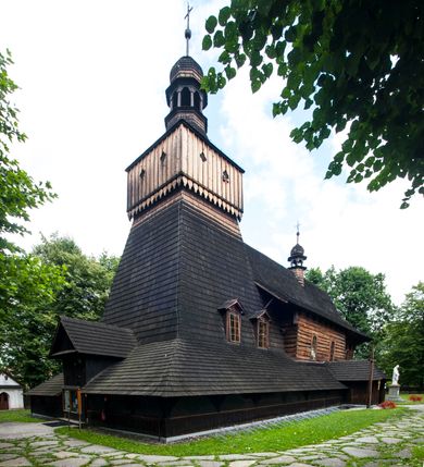 Zdjęcie nr 24: Drewniany kościół pw. św. Marcina w Jawiszowicach jest budowlą orientowaną, wzniesioną na zrąb. Do węższego prezbiterium zamkniętego trójbocznie przylega szersza nawa na rzucie zbliżonym do kwadratu. Od północy przy prezbiterium wybudowano zakrystię na planie wydłużonego prostokąta, a od zachodu wieżę w konstrukcji na słup na rzucie kwadratu. Zwieńczono ją izbicą z baniastym hełmem z latarnią. W przyziemiu wieży urządzono kruchtę. Nawę z prezbiterium nakryto jednokalenicowym dachem z więźbą w układzie storczykowym z przypustnicami (nadbitkami). W węższej części prezbiterialnej dach wsparty jest na trójkątnych zastrzałach widocznych na zewnątrz. Nad prezbiterium wznosi się sygnaturka w formie latarni z baniastym hełmem zwieńczonym krzyżem. Bryłę kościoła w całości otaczają arkadowe soboty z drewnianymi parapetami i z prześwitami wypełnionymi półprzeźroczystą pleksą. Na wysokości wejścia południowego do kościoła linię sobót wysunięto do przodu, dzięki czemu powstała pseudokruchta nakryta dachem siodłowym. Zarówno dach kościoła, jak i zakrystii, sobót oraz hełmy wieży i sygnaturki pokryte są gontem. Ściany nawy i prezbiterium utworzone z poziomo układanych bali przepruwają prostokątne okna z wpisanym łukiem półokrągłym, stanowiącym część stolarki okiennej. Na osi prezbiterium za ołtarzem głównym wycięto okulus. Wnętrze kościoła w nawie nakrywa płaski strop ze skośnym szalowaniem po bokach, a w prezbiterium pozorne sklepienie kolebkowe. Prezbiterium od nawy oddziela półokrągła tęcza z profilowaną belką, na której umieszczono grupę Ukrzyżowania. Całość wnętrza zdobi wielobarwna, ornamentalno-figuralna polichromia. Podłogę świątyni wyłożono kamiennymi płytami. W zachodniej części nawy urządzono chór muzyczny wsparty na dwóch drewnianych filarach z klatką schodową usytuowaną w południowo-zachodnim narożniku. Na chórze ustawiono prospekt organowy. Do wnętrza kościoła prowadzą dwa wejścia - od zachodu poprzez kruchtę w przyziemiu wieży oraz od południa z drewnianym portalem zamkniętym łukiem odcinkowym. Drewniany portal zamknięty łukiem odcinkowym prowadzi także z prezbiterium do zakrystii. Wypełniają go obite metalowymi płycinami i listwami drzwi. Własne wejście na zewnątrz posiada także zakrystia. Wnętrze prezbiterium w części wschodniej wypełnia architektoniczny ołtarz główny. Na ścianie północnej prezbiterium przy łuku tęczowym zawieszono ambonę, do której schody prowadzą z zakrystii. Pod skosem po obu stronach łuku tęczowego w narożnikach nawy ustawiono dwa ołtarze boczne, a pod chórem muzycznym dwa konfesjonały. W nawie stoją dwa rzędy ław kościelnych, a na jej ścianie północnej zawieszono na półeczkach feretrony procesyjne. Kościół otacza droga procesyjna wyłożona kamiennymi płytami, a cmentarz przykościelny zamyka drewniany parkan z dwiema bramkami wejściowymi.    