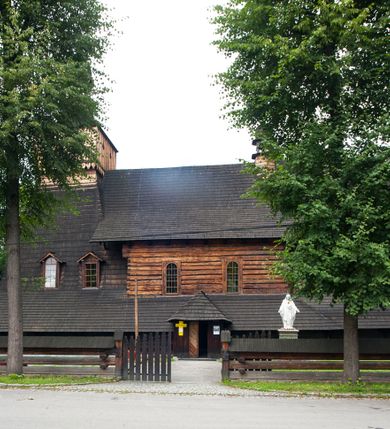 Zdjęcie nr 27: Drewniany kościół pw. św. Marcina w Jawiszowicach jest budowlą orientowaną, wzniesioną na zrąb. Do węższego prezbiterium zamkniętego trójbocznie przylega szersza nawa na rzucie zbliżonym do kwadratu. Od północy przy prezbiterium wybudowano zakrystię na planie wydłużonego prostokąta, a od zachodu wieżę w konstrukcji na słup na rzucie kwadratu. Zwieńczono ją izbicą z baniastym hełmem z latarnią. W przyziemiu wieży urządzono kruchtę. Nawę z prezbiterium nakryto jednokalenicowym dachem z więźbą w układzie storczykowym z przypustnicami (nadbitkami). W węższej części prezbiterialnej dach wsparty jest na trójkątnych zastrzałach widocznych na zewnątrz. Nad prezbiterium wznosi się sygnaturka w formie latarni z baniastym hełmem zwieńczonym krzyżem. Bryłę kościoła w całości otaczają arkadowe soboty z drewnianymi parapetami i z prześwitami wypełnionymi półprzeźroczystą pleksą. Na wysokości wejścia południowego do kościoła linię sobót wysunięto do przodu, dzięki czemu powstała pseudokruchta nakryta dachem siodłowym. Zarówno dach kościoła, jak i zakrystii, sobót oraz hełmy wieży i sygnaturki pokryte są gontem. Ściany nawy i prezbiterium utworzone z poziomo układanych bali przepruwają prostokątne okna z wpisanym łukiem półokrągłym, stanowiącym część stolarki okiennej. Na osi prezbiterium za ołtarzem głównym wycięto okulus. Wnętrze kościoła w nawie nakrywa płaski strop ze skośnym szalowaniem po bokach, a w prezbiterium pozorne sklepienie kolebkowe. Prezbiterium od nawy oddziela półokrągła tęcza z profilowaną belką, na której umieszczono grupę Ukrzyżowania. Całość wnętrza zdobi wielobarwna, ornamentalno-figuralna polichromia. Podłogę świątyni wyłożono kamiennymi płytami. W zachodniej części nawy urządzono chór muzyczny wsparty na dwóch drewnianych filarach z klatką schodową usytuowaną w południowo-zachodnim narożniku. Na chórze ustawiono prospekt organowy. Do wnętrza kościoła prowadzą dwa wejścia - od zachodu poprzez kruchtę w przyziemiu wieży oraz od południa z drewnianym portalem zamkniętym łukiem odcinkowym. Drewniany portal zamknięty łukiem odcinkowym prowadzi także z prezbiterium do zakrystii. Wypełniają go obite metalowymi płycinami i listwami drzwi. Własne wejście na zewnątrz posiada także zakrystia. Wnętrze prezbiterium w części wschodniej wypełnia architektoniczny ołtarz główny. Na ścianie północnej prezbiterium przy łuku tęczowym zawieszono ambonę, do której schody prowadzą z zakrystii. Pod skosem po obu stronach łuku tęczowego w narożnikach nawy ustawiono dwa ołtarze boczne, a pod chórem muzycznym dwa konfesjonały. W nawie stoją dwa rzędy ław kościelnych, a na jej ścianie północnej zawieszono na półeczkach feretrony procesyjne. Kościół otacza droga procesyjna wyłożona kamiennymi płytami, a cmentarz przykościelny zamyka drewniany parkan z dwiema bramkami wejściowymi.    