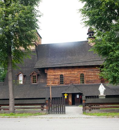 Zdjęcie nr 28: Drewniany kościół pw. św. Marcina w Jawiszowicach jest budowlą orientowaną, wzniesioną na zrąb. Do węższego prezbiterium zamkniętego trójbocznie przylega szersza nawa na rzucie zbliżonym do kwadratu. Od północy przy prezbiterium wybudowano zakrystię na planie wydłużonego prostokąta, a od zachodu wieżę w konstrukcji na słup na rzucie kwadratu. Zwieńczono ją izbicą z baniastym hełmem z latarnią. W przyziemiu wieży urządzono kruchtę. Nawę z prezbiterium nakryto jednokalenicowym dachem z więźbą w układzie storczykowym z przypustnicami (nadbitkami). W węższej części prezbiterialnej dach wsparty jest na trójkątnych zastrzałach widocznych na zewnątrz. Nad prezbiterium wznosi się sygnaturka w formie latarni z baniastym hełmem zwieńczonym krzyżem. Bryłę kościoła w całości otaczają arkadowe soboty z drewnianymi parapetami i z prześwitami wypełnionymi półprzeźroczystą pleksą. Na wysokości wejścia południowego do kościoła linię sobót wysunięto do przodu, dzięki czemu powstała pseudokruchta nakryta dachem siodłowym. Zarówno dach kościoła, jak i zakrystii, sobót oraz hełmy wieży i sygnaturki pokryte są gontem. Ściany nawy i prezbiterium utworzone z poziomo układanych bali przepruwają prostokątne okna z wpisanym łukiem półokrągłym, stanowiącym część stolarki okiennej. Na osi prezbiterium za ołtarzem głównym wycięto okulus. Wnętrze kościoła w nawie nakrywa płaski strop ze skośnym szalowaniem po bokach, a w prezbiterium pozorne sklepienie kolebkowe. Prezbiterium od nawy oddziela półokrągła tęcza z profilowaną belką, na której umieszczono grupę Ukrzyżowania. Całość wnętrza zdobi wielobarwna, ornamentalno-figuralna polichromia. Podłogę świątyni wyłożono kamiennymi płytami. W zachodniej części nawy urządzono chór muzyczny wsparty na dwóch drewnianych filarach z klatką schodową usytuowaną w południowo-zachodnim narożniku. Na chórze ustawiono prospekt organowy. Do wnętrza kościoła prowadzą dwa wejścia - od zachodu poprzez kruchtę w przyziemiu wieży oraz od południa z drewnianym portalem zamkniętym łukiem odcinkowym. Drewniany portal zamknięty łukiem odcinkowym prowadzi także z prezbiterium do zakrystii. Wypełniają go obite metalowymi płycinami i listwami drzwi. Własne wejście na zewnątrz posiada także zakrystia. Wnętrze prezbiterium w części wschodniej wypełnia architektoniczny ołtarz główny. Na ścianie północnej prezbiterium przy łuku tęczowym zawieszono ambonę, do której schody prowadzą z zakrystii. Pod skosem po obu stronach łuku tęczowego w narożnikach nawy ustawiono dwa ołtarze boczne, a pod chórem muzycznym dwa konfesjonały. W nawie stoją dwa rzędy ław kościelnych, a na jej ścianie północnej zawieszono na półeczkach feretrony procesyjne. Kościół otacza droga procesyjna wyłożona kamiennymi płytami, a cmentarz przykościelny zamyka drewniany parkan z dwiema bramkami wejściowymi.    