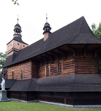 Zdjęcie nr 4: Drewniany kościół pw. św. Marcina w Jawiszowicach jest budowlą orientowaną, wzniesioną na zrąb. Do węższego prezbiterium zamkniętego trójbocznie przylega szersza nawa na rzucie zbliżonym do kwadratu. Od północy przy prezbiterium wybudowano zakrystię na planie wydłużonego prostokąta, a od zachodu wieżę w konstrukcji na słup na rzucie kwadratu. Zwieńczono ją izbicą z baniastym hełmem z latarnią. W przyziemiu wieży urządzono kruchtę. Nawę z prezbiterium nakryto jednokalenicowym dachem z więźbą w układzie storczykowym z przypustnicami (nadbitkami). W węższej części prezbiterialnej dach wsparty jest na trójkątnych zastrzałach widocznych na zewnątrz. Nad prezbiterium wznosi się sygnaturka w formie latarni z baniastym hełmem zwieńczonym krzyżem. Bryłę kościoła w całości otaczają arkadowe soboty z drewnianymi parapetami i z prześwitami wypełnionymi półprzeźroczystą pleksą. Na wysokości wejścia południowego do kościoła linię sobót wysunięto do przodu, dzięki czemu powstała pseudokruchta nakryta dachem siodłowym. Zarówno dach kościoła, jak i zakrystii, sobót oraz hełmy wieży i sygnaturki pokryte są gontem. Ściany nawy i prezbiterium utworzone z poziomo układanych bali przepruwają prostokątne okna z wpisanym łukiem półokrągłym, stanowiącym część stolarki okiennej. Na osi prezbiterium za ołtarzem głównym wycięto okulus. Wnętrze kościoła w nawie nakrywa płaski strop ze skośnym szalowaniem po bokach, a w prezbiterium pozorne sklepienie kolebkowe. Prezbiterium od nawy oddziela półokrągła tęcza z profilowaną belką, na której umieszczono grupę Ukrzyżowania. Całość wnętrza zdobi wielobarwna, ornamentalno-figuralna polichromia. Podłogę świątyni wyłożono kamiennymi płytami. W zachodniej części nawy urządzono chór muzyczny wsparty na dwóch drewnianych filarach z klatką schodową usytuowaną w południowo-zachodnim narożniku. Na chórze ustawiono prospekt organowy. Do wnętrza kościoła prowadzą dwa wejścia - od zachodu poprzez kruchtę w przyziemiu wieży oraz od południa z drewnianym portalem zamkniętym łukiem odcinkowym. Drewniany portal zamknięty łukiem odcinkowym prowadzi także z prezbiterium do zakrystii. Wypełniają go obite metalowymi płycinami i listwami drzwi. Własne wejście na zewnątrz posiada także zakrystia. Wnętrze prezbiterium w części wschodniej wypełnia architektoniczny ołtarz główny. Na ścianie północnej prezbiterium przy łuku tęczowym zawieszono ambonę, do której schody prowadzą z zakrystii. Pod skosem po obu stronach łuku tęczowego w narożnikach nawy ustawiono dwa ołtarze boczne, a pod chórem muzycznym dwa konfesjonały. W nawie stoją dwa rzędy ław kościelnych, a na jej ścianie północnej zawieszono na półeczkach feretrony procesyjne. Kościół otacza droga procesyjna wyłożona kamiennymi płytami, a cmentarz przykościelny zamyka drewniany parkan z dwiema bramkami wejściowymi.    