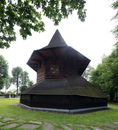 Zdjęcie nr 6: Drewniany kościół pw. św. Marcina w Jawiszowicach jest budowlą orientowaną, wzniesioną na zrąb. Do węższego prezbiterium zamkniętego trójbocznie przylega szersza nawa na rzucie zbliżonym do kwadratu. Od północy przy prezbiterium wybudowano zakrystię na planie wydłużonego prostokąta, a od zachodu wieżę w konstrukcji na słup na rzucie kwadratu. Zwieńczono ją izbicą z baniastym hełmem z latarnią. W przyziemiu wieży urządzono kruchtę. Nawę z prezbiterium nakryto jednokalenicowym dachem z więźbą w układzie storczykowym z przypustnicami (nadbitkami). W węższej części prezbiterialnej dach wsparty jest na trójkątnych zastrzałach widocznych na zewnątrz. Nad prezbiterium wznosi się sygnaturka w formie latarni z baniastym hełmem zwieńczonym krzyżem. Bryłę kościoła w całości otaczają arkadowe soboty z drewnianymi parapetami i z prześwitami wypełnionymi półprzeźroczystą pleksą. Na wysokości wejścia południowego do kościoła linię sobót wysunięto do przodu, dzięki czemu powstała pseudokruchta nakryta dachem siodłowym. Zarówno dach kościoła, jak i zakrystii, sobót oraz hełmy wieży i sygnaturki pokryte są gontem. Ściany nawy i prezbiterium utworzone z poziomo układanych bali przepruwają prostokątne okna z wpisanym łukiem półokrągłym, stanowiącym część stolarki okiennej. Na osi prezbiterium za ołtarzem głównym wycięto okulus. Wnętrze kościoła w nawie nakrywa płaski strop ze skośnym szalowaniem po bokach, a w prezbiterium pozorne sklepienie kolebkowe. Prezbiterium od nawy oddziela półokrągła tęcza z profilowaną belką, na której umieszczono grupę Ukrzyżowania. Całość wnętrza zdobi wielobarwna, ornamentalno-figuralna polichromia. Podłogę świątyni wyłożono kamiennymi płytami. W zachodniej części nawy urządzono chór muzyczny wsparty na dwóch drewnianych filarach z klatką schodową usytuowaną w południowo-zachodnim narożniku. Na chórze ustawiono prospekt organowy. Do wnętrza kościoła prowadzą dwa wejścia - od zachodu poprzez kruchtę w przyziemiu wieży oraz od południa z drewnianym portalem zamkniętym łukiem odcinkowym. Drewniany portal zamknięty łukiem odcinkowym prowadzi także z prezbiterium do zakrystii. Wypełniają go obite metalowymi płycinami i listwami drzwi. Własne wejście na zewnątrz posiada także zakrystia. Wnętrze prezbiterium w części wschodniej wypełnia architektoniczny ołtarz główny. Na ścianie północnej prezbiterium przy łuku tęczowym zawieszono ambonę, do której schody prowadzą z zakrystii. Pod skosem po obu stronach łuku tęczowego w narożnikach nawy ustawiono dwa ołtarze boczne, a pod chórem muzycznym dwa konfesjonały. W nawie stoją dwa rzędy ław kościelnych, a na jej ścianie północnej zawieszono na półeczkach feretrony procesyjne. Kościół otacza droga procesyjna wyłożona kamiennymi płytami, a cmentarz przykościelny zamyka drewniany parkan z dwiema bramkami wejściowymi.    