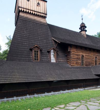 Zdjęcie nr 31: Drewniany kościół pw. św. Marcina w Jawiszowicach jest budowlą orientowaną, wzniesioną na zrąb. Do węższego prezbiterium zamkniętego trójbocznie przylega szersza nawa na rzucie zbliżonym do kwadratu. Od północy przy prezbiterium wybudowano zakrystię na planie wydłużonego prostokąta, a od zachodu wieżę w konstrukcji na słup na rzucie kwadratu. Zwieńczono ją izbicą z baniastym hełmem z latarnią. W przyziemiu wieży urządzono kruchtę. Nawę z prezbiterium nakryto jednokalenicowym dachem z więźbą w układzie storczykowym z przypustnicami (nadbitkami). W węższej części prezbiterialnej dach wsparty jest na trójkątnych zastrzałach widocznych na zewnątrz. Nad prezbiterium wznosi się sygnaturka w formie latarni z baniastym hełmem zwieńczonym krzyżem. Bryłę kościoła w całości otaczają arkadowe soboty z drewnianymi parapetami i z prześwitami wypełnionymi półprzeźroczystą pleksą. Na wysokości wejścia południowego do kościoła linię sobót wysunięto do przodu, dzięki czemu powstała pseudokruchta nakryta dachem siodłowym. Zarówno dach kościoła, jak i zakrystii, sobót oraz hełmy wieży i sygnaturki pokryte są gontem. Ściany nawy i prezbiterium utworzone z poziomo układanych bali przepruwają prostokątne okna z wpisanym łukiem półokrągłym, stanowiącym część stolarki okiennej. Na osi prezbiterium za ołtarzem głównym wycięto okulus. Wnętrze kościoła w nawie nakrywa płaski strop ze skośnym szalowaniem po bokach, a w prezbiterium pozorne sklepienie kolebkowe. Prezbiterium od nawy oddziela półokrągła tęcza z profilowaną belką, na której umieszczono grupę Ukrzyżowania. Całość wnętrza zdobi wielobarwna, ornamentalno-figuralna polichromia. Podłogę świątyni wyłożono kamiennymi płytami. W zachodniej części nawy urządzono chór muzyczny wsparty na dwóch drewnianych filarach z klatką schodową usytuowaną w południowo-zachodnim narożniku. Na chórze ustawiono prospekt organowy. Do wnętrza kościoła prowadzą dwa wejścia - od zachodu poprzez kruchtę w przyziemiu wieży oraz od południa z drewnianym portalem zamkniętym łukiem odcinkowym. Drewniany portal zamknięty łukiem odcinkowym prowadzi także z prezbiterium do zakrystii. Wypełniają go obite metalowymi płycinami i listwami drzwi. Własne wejście na zewnątrz posiada także zakrystia. Wnętrze prezbiterium w części wschodniej wypełnia architektoniczny ołtarz główny. Na ścianie północnej prezbiterium przy łuku tęczowym zawieszono ambonę, do której schody prowadzą z zakrystii. Pod skosem po obu stronach łuku tęczowego w narożnikach nawy ustawiono dwa ołtarze boczne, a pod chórem muzycznym dwa konfesjonały. W nawie stoją dwa rzędy ław kościelnych, a na jej ścianie północnej zawieszono na półeczkach feretrony procesyjne. Kościół otacza droga procesyjna wyłożona kamiennymi płytami, a cmentarz przykościelny zamyka drewniany parkan z dwiema bramkami wejściowymi.    