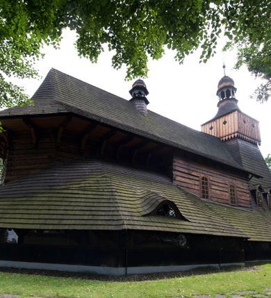 Zdjęcie nr 7: Drewniany kościół pw. św. Marcina w Jawiszowicach jest budowlą orientowaną, wzniesioną na zrąb. Do węższego prezbiterium zamkniętego trójbocznie przylega szersza nawa na rzucie zbliżonym do kwadratu. Od północy przy prezbiterium wybudowano zakrystię na planie wydłużonego prostokąta, a od zachodu wieżę w konstrukcji na słup na rzucie kwadratu. Zwieńczono ją izbicą z baniastym hełmem z latarnią. W przyziemiu wieży urządzono kruchtę. Nawę z prezbiterium nakryto jednokalenicowym dachem z więźbą w układzie storczykowym z przypustnicami (nadbitkami). W węższej części prezbiterialnej dach wsparty jest na trójkątnych zastrzałach widocznych na zewnątrz. Nad prezbiterium wznosi się sygnaturka w formie latarni z baniastym hełmem zwieńczonym krzyżem. Bryłę kościoła w całości otaczają arkadowe soboty z drewnianymi parapetami i z prześwitami wypełnionymi półprzeźroczystą pleksą. Na wysokości wejścia południowego do kościoła linię sobót wysunięto do przodu, dzięki czemu powstała pseudokruchta nakryta dachem siodłowym. Zarówno dach kościoła, jak i zakrystii, sobót oraz hełmy wieży i sygnaturki pokryte są gontem. Ściany nawy i prezbiterium utworzone z poziomo układanych bali przepruwają prostokątne okna z wpisanym łukiem półokrągłym, stanowiącym część stolarki okiennej. Na osi prezbiterium za ołtarzem głównym wycięto okulus. Wnętrze kościoła w nawie nakrywa płaski strop ze skośnym szalowaniem po bokach, a w prezbiterium pozorne sklepienie kolebkowe. Prezbiterium od nawy oddziela półokrągła tęcza z profilowaną belką, na której umieszczono grupę Ukrzyżowania. Całość wnętrza zdobi wielobarwna, ornamentalno-figuralna polichromia. Podłogę świątyni wyłożono kamiennymi płytami. W zachodniej części nawy urządzono chór muzyczny wsparty na dwóch drewnianych filarach z klatką schodową usytuowaną w południowo-zachodnim narożniku. Na chórze ustawiono prospekt organowy. Do wnętrza kościoła prowadzą dwa wejścia - od zachodu poprzez kruchtę w przyziemiu wieży oraz od południa z drewnianym portalem zamkniętym łukiem odcinkowym. Drewniany portal zamknięty łukiem odcinkowym prowadzi także z prezbiterium do zakrystii. Wypełniają go obite metalowymi płycinami i listwami drzwi. Własne wejście na zewnątrz posiada także zakrystia. Wnętrze prezbiterium w części wschodniej wypełnia architektoniczny ołtarz główny. Na ścianie północnej prezbiterium przy łuku tęczowym zawieszono ambonę, do której schody prowadzą z zakrystii. Pod skosem po obu stronach łuku tęczowego w narożnikach nawy ustawiono dwa ołtarze boczne, a pod chórem muzycznym dwa konfesjonały. W nawie stoją dwa rzędy ław kościelnych, a na jej ścianie północnej zawieszono na półeczkach feretrony procesyjne. Kościół otacza droga procesyjna wyłożona kamiennymi płytami, a cmentarz przykościelny zamyka drewniany parkan z dwiema bramkami wejściowymi.    