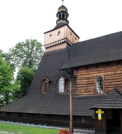 Zdjęcie nr 5: Drewniany kościół pw. św. Marcina w Jawiszowicach jest budowlą orientowaną, wzniesioną na zrąb. Do węższego prezbiterium zamkniętego trójbocznie przylega szersza nawa na rzucie zbliżonym do kwadratu. Od północy przy prezbiterium wybudowano zakrystię na planie wydłużonego prostokąta, a od zachodu wieżę w konstrukcji na słup na rzucie kwadratu. Zwieńczono ją izbicą z baniastym hełmem z latarnią. W przyziemiu wieży urządzono kruchtę. Nawę z prezbiterium nakryto jednokalenicowym dachem z więźbą w układzie storczykowym z przypustnicami (nadbitkami). W węższej części prezbiterialnej dach wsparty jest na trójkątnych zastrzałach widocznych na zewnątrz. Nad prezbiterium wznosi się sygnaturka w formie latarni z baniastym hełmem zwieńczonym krzyżem. Bryłę kościoła w całości otaczają arkadowe soboty z drewnianymi parapetami i z prześwitami wypełnionymi półprzeźroczystą pleksą. Na wysokości wejścia południowego do kościoła linię sobót wysunięto do przodu, dzięki czemu powstała pseudokruchta nakryta dachem siodłowym. Zarówno dach kościoła, jak i zakrystii, sobót oraz hełmy wieży i sygnaturki pokryte są gontem. Ściany nawy i prezbiterium utworzone z poziomo układanych bali przepruwają prostokątne okna z wpisanym łukiem półokrągłym, stanowiącym część stolarki okiennej. Na osi prezbiterium za ołtarzem głównym wycięto okulus. Wnętrze kościoła w nawie nakrywa płaski strop ze skośnym szalowaniem po bokach, a w prezbiterium pozorne sklepienie kolebkowe. Prezbiterium od nawy oddziela półokrągła tęcza z profilowaną belką, na której umieszczono grupę Ukrzyżowania. Całość wnętrza zdobi wielobarwna, ornamentalno-figuralna polichromia. Podłogę świątyni wyłożono kamiennymi płytami. W zachodniej części nawy urządzono chór muzyczny wsparty na dwóch drewnianych filarach z klatką schodową usytuowaną w południowo-zachodnim narożniku. Na chórze ustawiono prospekt organowy. Do wnętrza kościoła prowadzą dwa wejścia - od zachodu poprzez kruchtę w przyziemiu wieży oraz od południa z drewnianym portalem zamkniętym łukiem odcinkowym. Drewniany portal zamknięty łukiem odcinkowym prowadzi także z prezbiterium do zakrystii. Wypełniają go obite metalowymi płycinami i listwami drzwi. Własne wejście na zewnątrz posiada także zakrystia. Wnętrze prezbiterium w części wschodniej wypełnia architektoniczny ołtarz główny. Na ścianie północnej prezbiterium przy łuku tęczowym zawieszono ambonę, do której schody prowadzą z zakrystii. Pod skosem po obu stronach łuku tęczowego w narożnikach nawy ustawiono dwa ołtarze boczne, a pod chórem muzycznym dwa konfesjonały. W nawie stoją dwa rzędy ław kościelnych, a na jej ścianie północnej zawieszono na półeczkach feretrony procesyjne. Kościół otacza droga procesyjna wyłożona kamiennymi płytami, a cmentarz przykościelny zamyka drewniany parkan z dwiema bramkami wejściowymi.    