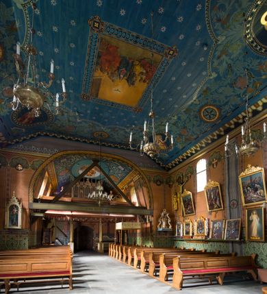 Zdjęcie nr 23: Drewniany kościół pw. św. Marcina w Jawiszowicach jest budowlą orientowaną, wzniesioną na zrąb. Do węższego prezbiterium zamkniętego trójbocznie przylega szersza nawa na rzucie zbliżonym do kwadratu. Od północy przy prezbiterium wybudowano zakrystię na planie wydłużonego prostokąta, a od zachodu wieżę w konstrukcji na słup na rzucie kwadratu. Zwieńczono ją izbicą z baniastym hełmem z latarnią. W przyziemiu wieży urządzono kruchtę. Nawę z prezbiterium nakryto jednokalenicowym dachem z więźbą w układzie storczykowym z przypustnicami (nadbitkami). W węższej części prezbiterialnej dach wsparty jest na trójkątnych zastrzałach widocznych na zewnątrz. Nad prezbiterium wznosi się sygnaturka w formie latarni z baniastym hełmem zwieńczonym krzyżem. Bryłę kościoła w całości otaczają arkadowe soboty z drewnianymi parapetami i z prześwitami wypełnionymi półprzeźroczystą pleksą. Na wysokości wejścia południowego do kościoła linię sobót wysunięto do przodu, dzięki czemu powstała pseudokruchta nakryta dachem siodłowym. Zarówno dach kościoła, jak i zakrystii, sobót oraz hełmy wieży i sygnaturki pokryte są gontem. Ściany nawy i prezbiterium utworzone z poziomo układanych bali przepruwają prostokątne okna z wpisanym łukiem półokrągłym, stanowiącym część stolarki okiennej. Na osi prezbiterium za ołtarzem głównym wycięto okulus. Wnętrze kościoła w nawie nakrywa płaski strop ze skośnym szalowaniem po bokach, a w prezbiterium pozorne sklepienie kolebkowe. Prezbiterium od nawy oddziela półokrągła tęcza z profilowaną belką, na której umieszczono grupę Ukrzyżowania. Całość wnętrza zdobi wielobarwna, ornamentalno-figuralna polichromia. Podłogę świątyni wyłożono kamiennymi płytami. W zachodniej części nawy urządzono chór muzyczny wsparty na dwóch drewnianych filarach z klatką schodową usytuowaną w południowo-zachodnim narożniku. Na chórze ustawiono prospekt organowy. Do wnętrza kościoła prowadzą dwa wejścia - od zachodu poprzez kruchtę w przyziemiu wieży oraz od południa z drewnianym portalem zamkniętym łukiem odcinkowym. Drewniany portal zamknięty łukiem odcinkowym prowadzi także z prezbiterium do zakrystii. Wypełniają go obite metalowymi płycinami i listwami drzwi. Własne wejście na zewnątrz posiada także zakrystia. Wnętrze prezbiterium w części wschodniej wypełnia architektoniczny ołtarz główny. Na ścianie północnej prezbiterium przy łuku tęczowym zawieszono ambonę, do której schody prowadzą z zakrystii. Pod skosem po obu stronach łuku tęczowego w narożnikach nawy ustawiono dwa ołtarze boczne, a pod chórem muzycznym dwa konfesjonały. W nawie stoją dwa rzędy ław kościelnych, a na jej ścianie północnej zawieszono na półeczkach feretrony procesyjne. Kościół otacza droga procesyjna wyłożona kamiennymi płytami, a cmentarz przykościelny zamyka drewniany parkan z dwiema bramkami wejściowymi.    