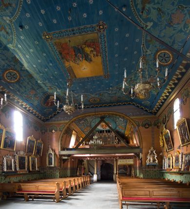 Zdjęcie nr 22: Drewniany kościół pw. św. Marcina w Jawiszowicach jest budowlą orientowaną, wzniesioną na zrąb. Do węższego prezbiterium zamkniętego trójbocznie przylega szersza nawa na rzucie zbliżonym do kwadratu. Od północy przy prezbiterium wybudowano zakrystię na planie wydłużonego prostokąta, a od zachodu wieżę w konstrukcji na słup na rzucie kwadratu. Zwieńczono ją izbicą z baniastym hełmem z latarnią. W przyziemiu wieży urządzono kruchtę. Nawę z prezbiterium nakryto jednokalenicowym dachem z więźbą w układzie storczykowym z przypustnicami (nadbitkami). W węższej części prezbiterialnej dach wsparty jest na trójkątnych zastrzałach widocznych na zewnątrz. Nad prezbiterium wznosi się sygnaturka w formie latarni z baniastym hełmem zwieńczonym krzyżem. Bryłę kościoła w całości otaczają arkadowe soboty z drewnianymi parapetami i z prześwitami wypełnionymi półprzeźroczystą pleksą. Na wysokości wejścia południowego do kościoła linię sobót wysunięto do przodu, dzięki czemu powstała pseudokruchta nakryta dachem siodłowym. Zarówno dach kościoła, jak i zakrystii, sobót oraz hełmy wieży i sygnaturki pokryte są gontem. Ściany nawy i prezbiterium utworzone z poziomo układanych bali przepruwają prostokątne okna z wpisanym łukiem półokrągłym, stanowiącym część stolarki okiennej. Na osi prezbiterium za ołtarzem głównym wycięto okulus. Wnętrze kościoła w nawie nakrywa płaski strop ze skośnym szalowaniem po bokach, a w prezbiterium pozorne sklepienie kolebkowe. Prezbiterium od nawy oddziela półokrągła tęcza z profilowaną belką, na której umieszczono grupę Ukrzyżowania. Całość wnętrza zdobi wielobarwna, ornamentalno-figuralna polichromia. Podłogę świątyni wyłożono kamiennymi płytami. W zachodniej części nawy urządzono chór muzyczny wsparty na dwóch drewnianych filarach z klatką schodową usytuowaną w południowo-zachodnim narożniku. Na chórze ustawiono prospekt organowy. Do wnętrza kościoła prowadzą dwa wejścia - od zachodu poprzez kruchtę w przyziemiu wieży oraz od południa z drewnianym portalem zamkniętym łukiem odcinkowym. Drewniany portal zamknięty łukiem odcinkowym prowadzi także z prezbiterium do zakrystii. Wypełniają go obite metalowymi płycinami i listwami drzwi. Własne wejście na zewnątrz posiada także zakrystia. Wnętrze prezbiterium w części wschodniej wypełnia architektoniczny ołtarz główny. Na ścianie północnej prezbiterium przy łuku tęczowym zawieszono ambonę, do której schody prowadzą z zakrystii. Pod skosem po obu stronach łuku tęczowego w narożnikach nawy ustawiono dwa ołtarze boczne, a pod chórem muzycznym dwa konfesjonały. W nawie stoją dwa rzędy ław kościelnych, a na jej ścianie północnej zawieszono na półeczkach feretrony procesyjne. Kościół otacza droga procesyjna wyłożona kamiennymi płytami, a cmentarz przykościelny zamyka drewniany parkan z dwiema bramkami wejściowymi.    