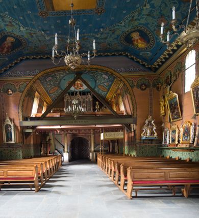 Zdjęcie nr 21: Drewniany kościół pw. św. Marcina w Jawiszowicach jest budowlą orientowaną, wzniesioną na zrąb. Do węższego prezbiterium zamkniętego trójbocznie przylega szersza nawa na rzucie zbliżonym do kwadratu. Od północy przy prezbiterium wybudowano zakrystię na planie wydłużonego prostokąta, a od zachodu wieżę w konstrukcji na słup na rzucie kwadratu. Zwieńczono ją izbicą z baniastym hełmem z latarnią. W przyziemiu wieży urządzono kruchtę. Nawę z prezbiterium nakryto jednokalenicowym dachem z więźbą w układzie storczykowym z przypustnicami (nadbitkami). W węższej części prezbiterialnej dach wsparty jest na trójkątnych zastrzałach widocznych na zewnątrz. Nad prezbiterium wznosi się sygnaturka w formie latarni z baniastym hełmem zwieńczonym krzyżem. Bryłę kościoła w całości otaczają arkadowe soboty z drewnianymi parapetami i z prześwitami wypełnionymi półprzeźroczystą pleksą. Na wysokości wejścia południowego do kościoła linię sobót wysunięto do przodu, dzięki czemu powstała pseudokruchta nakryta dachem siodłowym. Zarówno dach kościoła, jak i zakrystii, sobót oraz hełmy wieży i sygnaturki pokryte są gontem. Ściany nawy i prezbiterium utworzone z poziomo układanych bali przepruwają prostokątne okna z wpisanym łukiem półokrągłym, stanowiącym część stolarki okiennej. Na osi prezbiterium za ołtarzem głównym wycięto okulus. Wnętrze kościoła w nawie nakrywa płaski strop ze skośnym szalowaniem po bokach, a w prezbiterium pozorne sklepienie kolebkowe. Prezbiterium od nawy oddziela półokrągła tęcza z profilowaną belką, na której umieszczono grupę Ukrzyżowania. Całość wnętrza zdobi wielobarwna, ornamentalno-figuralna polichromia. Podłogę świątyni wyłożono kamiennymi płytami. W zachodniej części nawy urządzono chór muzyczny wsparty na dwóch drewnianych filarach z klatką schodową usytuowaną w południowo-zachodnim narożniku. Na chórze ustawiono prospekt organowy. Do wnętrza kościoła prowadzą dwa wejścia - od zachodu poprzez kruchtę w przyziemiu wieży oraz od południa z drewnianym portalem zamkniętym łukiem odcinkowym. Drewniany portal zamknięty łukiem odcinkowym prowadzi także z prezbiterium do zakrystii. Wypełniają go obite metalowymi płycinami i listwami drzwi. Własne wejście na zewnątrz posiada także zakrystia. Wnętrze prezbiterium w części wschodniej wypełnia architektoniczny ołtarz główny. Na ścianie północnej prezbiterium przy łuku tęczowym zawieszono ambonę, do której schody prowadzą z zakrystii. Pod skosem po obu stronach łuku tęczowego w narożnikach nawy ustawiono dwa ołtarze boczne, a pod chórem muzycznym dwa konfesjonały. W nawie stoją dwa rzędy ław kościelnych, a na jej ścianie północnej zawieszono na półeczkach feretrony procesyjne. Kościół otacza droga procesyjna wyłożona kamiennymi płytami, a cmentarz przykościelny zamyka drewniany parkan z dwiema bramkami wejściowymi.    