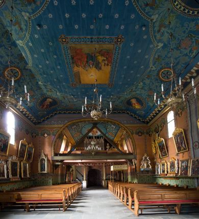 Zdjęcie nr 19: Drewniany kościół pw. św. Marcina w Jawiszowicach jest budowlą orientowaną, wzniesioną na zrąb. Do węższego prezbiterium zamkniętego trójbocznie przylega szersza nawa na rzucie zbliżonym do kwadratu. Od północy przy prezbiterium wybudowano zakrystię na planie wydłużonego prostokąta, a od zachodu wieżę w konstrukcji na słup na rzucie kwadratu. Zwieńczono ją izbicą z baniastym hełmem z latarnią. W przyziemiu wieży urządzono kruchtę. Nawę z prezbiterium nakryto jednokalenicowym dachem z więźbą w układzie storczykowym z przypustnicami (nadbitkami). W węższej części prezbiterialnej dach wsparty jest na trójkątnych zastrzałach widocznych na zewnątrz. Nad prezbiterium wznosi się sygnaturka w formie latarni z baniastym hełmem zwieńczonym krzyżem. Bryłę kościoła w całości otaczają arkadowe soboty z drewnianymi parapetami i z prześwitami wypełnionymi półprzeźroczystą pleksą. Na wysokości wejścia południowego do kościoła linię sobót wysunięto do przodu, dzięki czemu powstała pseudokruchta nakryta dachem siodłowym. Zarówno dach kościoła, jak i zakrystii, sobót oraz hełmy wieży i sygnaturki pokryte są gontem. Ściany nawy i prezbiterium utworzone z poziomo układanych bali przepruwają prostokątne okna z wpisanym łukiem półokrągłym, stanowiącym część stolarki okiennej. Na osi prezbiterium za ołtarzem głównym wycięto okulus. Wnętrze kościoła w nawie nakrywa płaski strop ze skośnym szalowaniem po bokach, a w prezbiterium pozorne sklepienie kolebkowe. Prezbiterium od nawy oddziela półokrągła tęcza z profilowaną belką, na której umieszczono grupę Ukrzyżowania. Całość wnętrza zdobi wielobarwna, ornamentalno-figuralna polichromia. Podłogę świątyni wyłożono kamiennymi płytami. W zachodniej części nawy urządzono chór muzyczny wsparty na dwóch drewnianych filarach z klatką schodową usytuowaną w południowo-zachodnim narożniku. Na chórze ustawiono prospekt organowy. Do wnętrza kościoła prowadzą dwa wejścia - od zachodu poprzez kruchtę w przyziemiu wieży oraz od południa z drewnianym portalem zamkniętym łukiem odcinkowym. Drewniany portal zamknięty łukiem odcinkowym prowadzi także z prezbiterium do zakrystii. Wypełniają go obite metalowymi płycinami i listwami drzwi. Własne wejście na zewnątrz posiada także zakrystia. Wnętrze prezbiterium w części wschodniej wypełnia architektoniczny ołtarz główny. Na ścianie północnej prezbiterium przy łuku tęczowym zawieszono ambonę, do której schody prowadzą z zakrystii. Pod skosem po obu stronach łuku tęczowego w narożnikach nawy ustawiono dwa ołtarze boczne, a pod chórem muzycznym dwa konfesjonały. W nawie stoją dwa rzędy ław kościelnych, a na jej ścianie północnej zawieszono na półeczkach feretrony procesyjne. Kościół otacza droga procesyjna wyłożona kamiennymi płytami, a cmentarz przykościelny zamyka drewniany parkan z dwiema bramkami wejściowymi.    