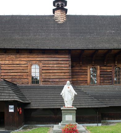 Zdjęcie nr 30: Drewniany kościół pw. św. Marcina w Jawiszowicach jest budowlą orientowaną, wzniesioną na zrąb. Do węższego prezbiterium zamkniętego trójbocznie przylega szersza nawa na rzucie zbliżonym do kwadratu. Od północy przy prezbiterium wybudowano zakrystię na planie wydłużonego prostokąta, a od zachodu wieżę w konstrukcji na słup na rzucie kwadratu. Zwieńczono ją izbicą z baniastym hełmem z latarnią. W przyziemiu wieży urządzono kruchtę. Nawę z prezbiterium nakryto jednokalenicowym dachem z więźbą w układzie storczykowym z przypustnicami (nadbitkami). W węższej części prezbiterialnej dach wsparty jest na trójkątnych zastrzałach widocznych na zewnątrz. Nad prezbiterium wznosi się sygnaturka w formie latarni z baniastym hełmem zwieńczonym krzyżem. Bryłę kościoła w całości otaczają arkadowe soboty z drewnianymi parapetami i z prześwitami wypełnionymi półprzeźroczystą pleksą. Na wysokości wejścia południowego do kościoła linię sobót wysunięto do przodu, dzięki czemu powstała pseudokruchta nakryta dachem siodłowym. Zarówno dach kościoła, jak i zakrystii, sobót oraz hełmy wieży i sygnaturki pokryte są gontem. Ściany nawy i prezbiterium utworzone z poziomo układanych bali przepruwają prostokątne okna z wpisanym łukiem półokrągłym, stanowiącym część stolarki okiennej. Na osi prezbiterium za ołtarzem głównym wycięto okulus. Wnętrze kościoła w nawie nakrywa płaski strop ze skośnym szalowaniem po bokach, a w prezbiterium pozorne sklepienie kolebkowe. Prezbiterium od nawy oddziela półokrągła tęcza z profilowaną belką, na której umieszczono grupę Ukrzyżowania. Całość wnętrza zdobi wielobarwna, ornamentalno-figuralna polichromia. Podłogę świątyni wyłożono kamiennymi płytami. W zachodniej części nawy urządzono chór muzyczny wsparty na dwóch drewnianych filarach z klatką schodową usytuowaną w południowo-zachodnim narożniku. Na chórze ustawiono prospekt organowy. Do wnętrza kościoła prowadzą dwa wejścia - od zachodu poprzez kruchtę w przyziemiu wieży oraz od południa z drewnianym portalem zamkniętym łukiem odcinkowym. Drewniany portal zamknięty łukiem odcinkowym prowadzi także z prezbiterium do zakrystii. Wypełniają go obite metalowymi płycinami i listwami drzwi. Własne wejście na zewnątrz posiada także zakrystia. Wnętrze prezbiterium w części wschodniej wypełnia architektoniczny ołtarz główny. Na ścianie północnej prezbiterium przy łuku tęczowym zawieszono ambonę, do której schody prowadzą z zakrystii. Pod skosem po obu stronach łuku tęczowego w narożnikach nawy ustawiono dwa ołtarze boczne, a pod chórem muzycznym dwa konfesjonały. W nawie stoją dwa rzędy ław kościelnych, a na jej ścianie północnej zawieszono na półeczkach feretrony procesyjne. Kościół otacza droga procesyjna wyłożona kamiennymi płytami, a cmentarz przykościelny zamyka drewniany parkan z dwiema bramkami wejściowymi.    