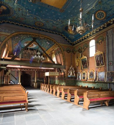 Zdjęcie nr 25: Drewniany kościół pw. św. Marcina w Jawiszowicach jest budowlą orientowaną, wzniesioną na zrąb. Do węższego prezbiterium zamkniętego trójbocznie przylega szersza nawa na rzucie zbliżonym do kwadratu. Od północy przy prezbiterium wybudowano zakrystię na planie wydłużonego prostokąta, a od zachodu wieżę w konstrukcji na słup na rzucie kwadratu. Zwieńczono ją izbicą z baniastym hełmem z latarnią. W przyziemiu wieży urządzono kruchtę. Nawę z prezbiterium nakryto jednokalenicowym dachem z więźbą w układzie storczykowym z przypustnicami (nadbitkami). W węższej części prezbiterialnej dach wsparty jest na trójkątnych zastrzałach widocznych na zewnątrz. Nad prezbiterium wznosi się sygnaturka w formie latarni z baniastym hełmem zwieńczonym krzyżem. Bryłę kościoła w całości otaczają arkadowe soboty z drewnianymi parapetami i z prześwitami wypełnionymi półprzeźroczystą pleksą. Na wysokości wejścia południowego do kościoła linię sobót wysunięto do przodu, dzięki czemu powstała pseudokruchta nakryta dachem siodłowym. Zarówno dach kościoła, jak i zakrystii, sobót oraz hełmy wieży i sygnaturki pokryte są gontem. Ściany nawy i prezbiterium utworzone z poziomo układanych bali przepruwają prostokątne okna z wpisanym łukiem półokrągłym, stanowiącym część stolarki okiennej. Na osi prezbiterium za ołtarzem głównym wycięto okulus. Wnętrze kościoła w nawie nakrywa płaski strop ze skośnym szalowaniem po bokach, a w prezbiterium pozorne sklepienie kolebkowe. Prezbiterium od nawy oddziela półokrągła tęcza z profilowaną belką, na której umieszczono grupę Ukrzyżowania. Całość wnętrza zdobi wielobarwna, ornamentalno-figuralna polichromia. Podłogę świątyni wyłożono kamiennymi płytami. W zachodniej części nawy urządzono chór muzyczny wsparty na dwóch drewnianych filarach z klatką schodową usytuowaną w południowo-zachodnim narożniku. Na chórze ustawiono prospekt organowy. Do wnętrza kościoła prowadzą dwa wejścia - od zachodu poprzez kruchtę w przyziemiu wieży oraz od południa z drewnianym portalem zamkniętym łukiem odcinkowym. Drewniany portal zamknięty łukiem odcinkowym prowadzi także z prezbiterium do zakrystii. Wypełniają go obite metalowymi płycinami i listwami drzwi. Własne wejście na zewnątrz posiada także zakrystia. Wnętrze prezbiterium w części wschodniej wypełnia architektoniczny ołtarz główny. Na ścianie północnej prezbiterium przy łuku tęczowym zawieszono ambonę, do której schody prowadzą z zakrystii. Pod skosem po obu stronach łuku tęczowego w narożnikach nawy ustawiono dwa ołtarze boczne, a pod chórem muzycznym dwa konfesjonały. W nawie stoją dwa rzędy ław kościelnych, a na jej ścianie północnej zawieszono na półeczkach feretrony procesyjne. Kościół otacza droga procesyjna wyłożona kamiennymi płytami, a cmentarz przykościelny zamyka drewniany parkan z dwiema bramkami wejściowymi.    