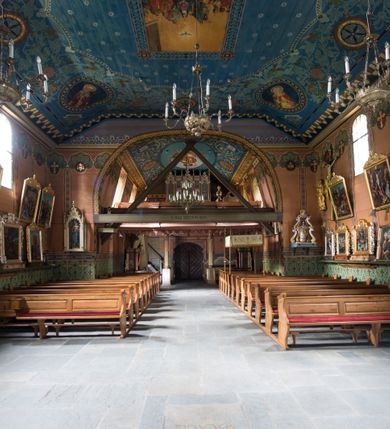 Zdjęcie nr 20: Drewniany kościół pw. św. Marcina w Jawiszowicach jest budowlą orientowaną, wzniesioną na zrąb. Do węższego prezbiterium zamkniętego trójbocznie przylega szersza nawa na rzucie zbliżonym do kwadratu. Od północy przy prezbiterium wybudowano zakrystię na planie wydłużonego prostokąta, a od zachodu wieżę w konstrukcji na słup na rzucie kwadratu. Zwieńczono ją izbicą z baniastym hełmem z latarnią. W przyziemiu wieży urządzono kruchtę. Nawę z prezbiterium nakryto jednokalenicowym dachem z więźbą w układzie storczykowym z przypustnicami (nadbitkami). W węższej części prezbiterialnej dach wsparty jest na trójkątnych zastrzałach widocznych na zewnątrz. Nad prezbiterium wznosi się sygnaturka w formie latarni z baniastym hełmem zwieńczonym krzyżem. Bryłę kościoła w całości otaczają arkadowe soboty z drewnianymi parapetami i z prześwitami wypełnionymi półprzeźroczystą pleksą. Na wysokości wejścia południowego do kościoła linię sobót wysunięto do przodu, dzięki czemu powstała pseudokruchta nakryta dachem siodłowym. Zarówno dach kościoła, jak i zakrystii, sobót oraz hełmy wieży i sygnaturki pokryte są gontem. Ściany nawy i prezbiterium utworzone z poziomo układanych bali przepruwają prostokątne okna z wpisanym łukiem półokrągłym, stanowiącym część stolarki okiennej. Na osi prezbiterium za ołtarzem głównym wycięto okulus. Wnętrze kościoła w nawie nakrywa płaski strop ze skośnym szalowaniem po bokach, a w prezbiterium pozorne sklepienie kolebkowe. Prezbiterium od nawy oddziela półokrągła tęcza z profilowaną belką, na której umieszczono grupę Ukrzyżowania. Całość wnętrza zdobi wielobarwna, ornamentalno-figuralna polichromia. Podłogę świątyni wyłożono kamiennymi płytami. W zachodniej części nawy urządzono chór muzyczny wsparty na dwóch drewnianych filarach z klatką schodową usytuowaną w południowo-zachodnim narożniku. Na chórze ustawiono prospekt organowy. Do wnętrza kościoła prowadzą dwa wejścia - od zachodu poprzez kruchtę w przyziemiu wieży oraz od południa z drewnianym portalem zamkniętym łukiem odcinkowym. Drewniany portal zamknięty łukiem odcinkowym prowadzi także z prezbiterium do zakrystii. Wypełniają go obite metalowymi płycinami i listwami drzwi. Własne wejście na zewnątrz posiada także zakrystia. Wnętrze prezbiterium w części wschodniej wypełnia architektoniczny ołtarz główny. Na ścianie północnej prezbiterium przy łuku tęczowym zawieszono ambonę, do której schody prowadzą z zakrystii. Pod skosem po obu stronach łuku tęczowego w narożnikach nawy ustawiono dwa ołtarze boczne, a pod chórem muzycznym dwa konfesjonały. W nawie stoją dwa rzędy ław kościelnych, a na jej ścianie północnej zawieszono na półeczkach feretrony procesyjne. Kościół otacza droga procesyjna wyłożona kamiennymi płytami, a cmentarz przykościelny zamyka drewniany parkan z dwiema bramkami wejściowymi.    