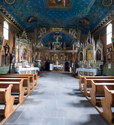 Zdjęcie nr 15: Drewniany kościół pw. św. Marcina w Jawiszowicach jest budowlą orientowaną, wzniesioną na zrąb. Do węższego prezbiterium zamkniętego trójbocznie przylega szersza nawa na rzucie zbliżonym do kwadratu. Od północy przy prezbiterium wybudowano zakrystię na planie wydłużonego prostokąta, a od zachodu wieżę w konstrukcji na słup na rzucie kwadratu. Zwieńczono ją izbicą z baniastym hełmem z latarnią. W przyziemiu wieży urządzono kruchtę. Nawę z prezbiterium nakryto jednokalenicowym dachem z więźbą w układzie storczykowym z przypustnicami (nadbitkami). W węższej części prezbiterialnej dach wsparty jest na trójkątnych zastrzałach widocznych na zewnątrz. Nad prezbiterium wznosi się sygnaturka w formie latarni z baniastym hełmem zwieńczonym krzyżem. Bryłę kościoła w całości otaczają arkadowe soboty z drewnianymi parapetami i z prześwitami wypełnionymi półprzeźroczystą pleksą. Na wysokości wejścia południowego do kościoła linię sobót wysunięto do przodu, dzięki czemu powstała pseudokruchta nakryta dachem siodłowym. Zarówno dach kościoła, jak i zakrystii, sobót oraz hełmy wieży i sygnaturki pokryte są gontem. Ściany nawy i prezbiterium utworzone z poziomo układanych bali przepruwają prostokątne okna z wpisanym łukiem półokrągłym, stanowiącym część stolarki okiennej. Na osi prezbiterium za ołtarzem głównym wycięto okulus. Wnętrze kościoła w nawie nakrywa płaski strop ze skośnym szalowaniem po bokach, a w prezbiterium pozorne sklepienie kolebkowe. Prezbiterium od nawy oddziela półokrągła tęcza z profilowaną belką, na której umieszczono grupę Ukrzyżowania. Całość wnętrza zdobi wielobarwna, ornamentalno-figuralna polichromia. Podłogę świątyni wyłożono kamiennymi płytami. W zachodniej części nawy urządzono chór muzyczny wsparty na dwóch drewnianych filarach z klatką schodową usytuowaną w południowo-zachodnim narożniku. Na chórze ustawiono prospekt organowy. Do wnętrza kościoła prowadzą dwa wejścia - od zachodu poprzez kruchtę w przyziemiu wieży oraz od południa z drewnianym portalem zamkniętym łukiem odcinkowym. Drewniany portal zamknięty łukiem odcinkowym prowadzi także z prezbiterium do zakrystii. Wypełniają go obite metalowymi płycinami i listwami drzwi. Własne wejście na zewnątrz posiada także zakrystia. Wnętrze prezbiterium w części wschodniej wypełnia architektoniczny ołtarz główny. Na ścianie północnej prezbiterium przy łuku tęczowym zawieszono ambonę, do której schody prowadzą z zakrystii. Pod skosem po obu stronach łuku tęczowego w narożnikach nawy ustawiono dwa ołtarze boczne, a pod chórem muzycznym dwa konfesjonały. W nawie stoją dwa rzędy ław kościelnych, a na jej ścianie północnej zawieszono na półeczkach feretrony procesyjne. Kościół otacza droga procesyjna wyłożona kamiennymi płytami, a cmentarz przykościelny zamyka drewniany parkan z dwiema bramkami wejściowymi.    