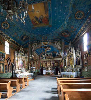 Zdjęcie nr 14: Drewniany kościół pw. św. Marcina w Jawiszowicach jest budowlą orientowaną, wzniesioną na zrąb. Do węższego prezbiterium zamkniętego trójbocznie przylega szersza nawa na rzucie zbliżonym do kwadratu. Od północy przy prezbiterium wybudowano zakrystię na planie wydłużonego prostokąta, a od zachodu wieżę w konstrukcji na słup na rzucie kwadratu. Zwieńczono ją izbicą z baniastym hełmem z latarnią. W przyziemiu wieży urządzono kruchtę. Nawę z prezbiterium nakryto jednokalenicowym dachem z więźbą w układzie storczykowym z przypustnicami (nadbitkami). W węższej części prezbiterialnej dach wsparty jest na trójkątnych zastrzałach widocznych na zewnątrz. Nad prezbiterium wznosi się sygnaturka w formie latarni z baniastym hełmem zwieńczonym krzyżem. Bryłę kościoła w całości otaczają arkadowe soboty z drewnianymi parapetami i z prześwitami wypełnionymi półprzeźroczystą pleksą. Na wysokości wejścia południowego do kościoła linię sobót wysunięto do przodu, dzięki czemu powstała pseudokruchta nakryta dachem siodłowym. Zarówno dach kościoła, jak i zakrystii, sobót oraz hełmy wieży i sygnaturki pokryte są gontem. Ściany nawy i prezbiterium utworzone z poziomo układanych bali przepruwają prostokątne okna z wpisanym łukiem półokrągłym, stanowiącym część stolarki okiennej. Na osi prezbiterium za ołtarzem głównym wycięto okulus. Wnętrze kościoła w nawie nakrywa płaski strop ze skośnym szalowaniem po bokach, a w prezbiterium pozorne sklepienie kolebkowe. Prezbiterium od nawy oddziela półokrągła tęcza z profilowaną belką, na której umieszczono grupę Ukrzyżowania. Całość wnętrza zdobi wielobarwna, ornamentalno-figuralna polichromia. Podłogę świątyni wyłożono kamiennymi płytami. W zachodniej części nawy urządzono chór muzyczny wsparty na dwóch drewnianych filarach z klatką schodową usytuowaną w południowo-zachodnim narożniku. Na chórze ustawiono prospekt organowy. Do wnętrza kościoła prowadzą dwa wejścia - od zachodu poprzez kruchtę w przyziemiu wieży oraz od południa z drewnianym portalem zamkniętym łukiem odcinkowym. Drewniany portal zamknięty łukiem odcinkowym prowadzi także z prezbiterium do zakrystii. Wypełniają go obite metalowymi płycinami i listwami drzwi. Własne wejście na zewnątrz posiada także zakrystia. Wnętrze prezbiterium w części wschodniej wypełnia architektoniczny ołtarz główny. Na ścianie północnej prezbiterium przy łuku tęczowym zawieszono ambonę, do której schody prowadzą z zakrystii. Pod skosem po obu stronach łuku tęczowego w narożnikach nawy ustawiono dwa ołtarze boczne, a pod chórem muzycznym dwa konfesjonały. W nawie stoją dwa rzędy ław kościelnych, a na jej ścianie północnej zawieszono na półeczkach feretrony procesyjne. Kościół otacza droga procesyjna wyłożona kamiennymi płytami, a cmentarz przykościelny zamyka drewniany parkan z dwiema bramkami wejściowymi.    