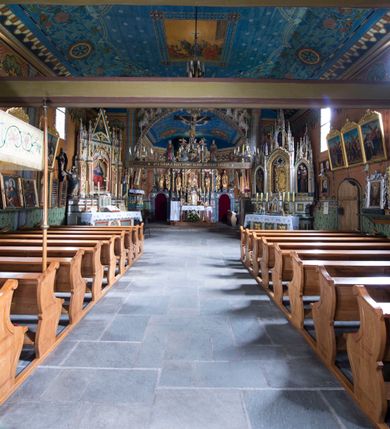 Zdjęcie nr 11: Drewniany kościół pw. św. Marcina w Jawiszowicach jest budowlą orientowaną, wzniesioną na zrąb. Do węższego prezbiterium zamkniętego trójbocznie przylega szersza nawa na rzucie zbliżonym do kwadratu. Od północy przy prezbiterium wybudowano zakrystię na planie wydłużonego prostokąta, a od zachodu wieżę w konstrukcji na słup na rzucie kwadratu. Zwieńczono ją izbicą z baniastym hełmem z latarnią. W przyziemiu wieży urządzono kruchtę. Nawę z prezbiterium nakryto jednokalenicowym dachem z więźbą w układzie storczykowym z przypustnicami (nadbitkami). W węższej części prezbiterialnej dach wsparty jest na trójkątnych zastrzałach widocznych na zewnątrz. Nad prezbiterium wznosi się sygnaturka w formie latarni z baniastym hełmem zwieńczonym krzyżem. Bryłę kościoła w całości otaczają arkadowe soboty z drewnianymi parapetami i z prześwitami wypełnionymi półprzeźroczystą pleksą. Na wysokości wejścia południowego do kościoła linię sobót wysunięto do przodu, dzięki czemu powstała pseudokruchta nakryta dachem siodłowym. Zarówno dach kościoła, jak i zakrystii, sobót oraz hełmy wieży i sygnaturki pokryte są gontem. Ściany nawy i prezbiterium utworzone z poziomo układanych bali przepruwają prostokątne okna z wpisanym łukiem półokrągłym, stanowiącym część stolarki okiennej. Na osi prezbiterium za ołtarzem głównym wycięto okulus. Wnętrze kościoła w nawie nakrywa płaski strop ze skośnym szalowaniem po bokach, a w prezbiterium pozorne sklepienie kolebkowe. Prezbiterium od nawy oddziela półokrągła tęcza z profilowaną belką, na której umieszczono grupę Ukrzyżowania. Całość wnętrza zdobi wielobarwna, ornamentalno-figuralna polichromia. Podłogę świątyni wyłożono kamiennymi płytami. W zachodniej części nawy urządzono chór muzyczny wsparty na dwóch drewnianych filarach z klatką schodową usytuowaną w południowo-zachodnim narożniku. Na chórze ustawiono prospekt organowy. Do wnętrza kościoła prowadzą dwa wejścia - od zachodu poprzez kruchtę w przyziemiu wieży oraz od południa z drewnianym portalem zamkniętym łukiem odcinkowym. Drewniany portal zamknięty łukiem odcinkowym prowadzi także z prezbiterium do zakrystii. Wypełniają go obite metalowymi płycinami i listwami drzwi. Własne wejście na zewnątrz posiada także zakrystia. Wnętrze prezbiterium w części wschodniej wypełnia architektoniczny ołtarz główny. Na ścianie północnej prezbiterium przy łuku tęczowym zawieszono ambonę, do której schody prowadzą z zakrystii. Pod skosem po obu stronach łuku tęczowego w narożnikach nawy ustawiono dwa ołtarze boczne, a pod chórem muzycznym dwa konfesjonały. W nawie stoją dwa rzędy ław kościelnych, a na jej ścianie północnej zawieszono na półeczkach feretrony procesyjne. Kościół otacza droga procesyjna wyłożona kamiennymi płytami, a cmentarz przykościelny zamyka drewniany parkan z dwiema bramkami wejściowymi.    