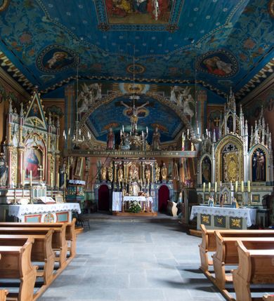 Zdjęcie nr 16: Drewniany kościół pw. św. Marcina w Jawiszowicach jest budowlą orientowaną, wzniesioną na zrąb. Do węższego prezbiterium zamkniętego trójbocznie przylega szersza nawa na rzucie zbliżonym do kwadratu. Od północy przy prezbiterium wybudowano zakrystię na planie wydłużonego prostokąta, a od zachodu wieżę w konstrukcji na słup na rzucie kwadratu. Zwieńczono ją izbicą z baniastym hełmem z latarnią. W przyziemiu wieży urządzono kruchtę. Nawę z prezbiterium nakryto jednokalenicowym dachem z więźbą w układzie storczykowym z przypustnicami (nadbitkami). W węższej części prezbiterialnej dach wsparty jest na trójkątnych zastrzałach widocznych na zewnątrz. Nad prezbiterium wznosi się sygnaturka w formie latarni z baniastym hełmem zwieńczonym krzyżem. Bryłę kościoła w całości otaczają arkadowe soboty z drewnianymi parapetami i z prześwitami wypełnionymi półprzeźroczystą pleksą. Na wysokości wejścia południowego do kościoła linię sobót wysunięto do przodu, dzięki czemu powstała pseudokruchta nakryta dachem siodłowym. Zarówno dach kościoła, jak i zakrystii, sobót oraz hełmy wieży i sygnaturki pokryte są gontem. Ściany nawy i prezbiterium utworzone z poziomo układanych bali przepruwają prostokątne okna z wpisanym łukiem półokrągłym, stanowiącym część stolarki okiennej. Na osi prezbiterium za ołtarzem głównym wycięto okulus. Wnętrze kościoła w nawie nakrywa płaski strop ze skośnym szalowaniem po bokach, a w prezbiterium pozorne sklepienie kolebkowe. Prezbiterium od nawy oddziela półokrągła tęcza z profilowaną belką, na której umieszczono grupę Ukrzyżowania. Całość wnętrza zdobi wielobarwna, ornamentalno-figuralna polichromia. Podłogę świątyni wyłożono kamiennymi płytami. W zachodniej części nawy urządzono chór muzyczny wsparty na dwóch drewnianych filarach z klatką schodową usytuowaną w południowo-zachodnim narożniku. Na chórze ustawiono prospekt organowy. Do wnętrza kościoła prowadzą dwa wejścia - od zachodu poprzez kruchtę w przyziemiu wieży oraz od południa z drewnianym portalem zamkniętym łukiem odcinkowym. Drewniany portal zamknięty łukiem odcinkowym prowadzi także z prezbiterium do zakrystii. Wypełniają go obite metalowymi płycinami i listwami drzwi. Własne wejście na zewnątrz posiada także zakrystia. Wnętrze prezbiterium w części wschodniej wypełnia architektoniczny ołtarz główny. Na ścianie północnej prezbiterium przy łuku tęczowym zawieszono ambonę, do której schody prowadzą z zakrystii. Pod skosem po obu stronach łuku tęczowego w narożnikach nawy ustawiono dwa ołtarze boczne, a pod chórem muzycznym dwa konfesjonały. W nawie stoją dwa rzędy ław kościelnych, a na jej ścianie północnej zawieszono na półeczkach feretrony procesyjne. Kościół otacza droga procesyjna wyłożona kamiennymi płytami, a cmentarz przykościelny zamyka drewniany parkan z dwiema bramkami wejściowymi.    