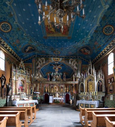 Zdjęcie nr 12: Drewniany kościół pw. św. Marcina w Jawiszowicach jest budowlą orientowaną, wzniesioną na zrąb. Do węższego prezbiterium zamkniętego trójbocznie przylega szersza nawa na rzucie zbliżonym do kwadratu. Od północy przy prezbiterium wybudowano zakrystię na planie wydłużonego prostokąta, a od zachodu wieżę w konstrukcji na słup na rzucie kwadratu. Zwieńczono ją izbicą z baniastym hełmem z latarnią. W przyziemiu wieży urządzono kruchtę. Nawę z prezbiterium nakryto jednokalenicowym dachem z więźbą w układzie storczykowym z przypustnicami (nadbitkami). W węższej części prezbiterialnej dach wsparty jest na trójkątnych zastrzałach widocznych na zewnątrz. Nad prezbiterium wznosi się sygnaturka w formie latarni z baniastym hełmem zwieńczonym krzyżem. Bryłę kościoła w całości otaczają arkadowe soboty z drewnianymi parapetami i z prześwitami wypełnionymi półprzeźroczystą pleksą. Na wysokości wejścia południowego do kościoła linię sobót wysunięto do przodu, dzięki czemu powstała pseudokruchta nakryta dachem siodłowym. Zarówno dach kościoła, jak i zakrystii, sobót oraz hełmy wieży i sygnaturki pokryte są gontem. Ściany nawy i prezbiterium utworzone z poziomo układanych bali przepruwają prostokątne okna z wpisanym łukiem półokrągłym, stanowiącym część stolarki okiennej. Na osi prezbiterium za ołtarzem głównym wycięto okulus. Wnętrze kościoła w nawie nakrywa płaski strop ze skośnym szalowaniem po bokach, a w prezbiterium pozorne sklepienie kolebkowe. Prezbiterium od nawy oddziela półokrągła tęcza z profilowaną belką, na której umieszczono grupę Ukrzyżowania. Całość wnętrza zdobi wielobarwna, ornamentalno-figuralna polichromia. Podłogę świątyni wyłożono kamiennymi płytami. W zachodniej części nawy urządzono chór muzyczny wsparty na dwóch drewnianych filarach z klatką schodową usytuowaną w południowo-zachodnim narożniku. Na chórze ustawiono prospekt organowy. Do wnętrza kościoła prowadzą dwa wejścia - od zachodu poprzez kruchtę w przyziemiu wieży oraz od południa z drewnianym portalem zamkniętym łukiem odcinkowym. Drewniany portal zamknięty łukiem odcinkowym prowadzi także z prezbiterium do zakrystii. Wypełniają go obite metalowymi płycinami i listwami drzwi. Własne wejście na zewnątrz posiada także zakrystia. Wnętrze prezbiterium w części wschodniej wypełnia architektoniczny ołtarz główny. Na ścianie północnej prezbiterium przy łuku tęczowym zawieszono ambonę, do której schody prowadzą z zakrystii. Pod skosem po obu stronach łuku tęczowego w narożnikach nawy ustawiono dwa ołtarze boczne, a pod chórem muzycznym dwa konfesjonały. W nawie stoją dwa rzędy ław kościelnych, a na jej ścianie północnej zawieszono na półeczkach feretrony procesyjne. Kościół otacza droga procesyjna wyłożona kamiennymi płytami, a cmentarz przykościelny zamyka drewniany parkan z dwiema bramkami wejściowymi.    