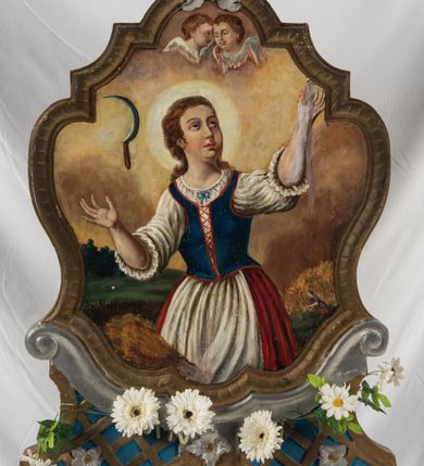 Zdjęcie nr 1: Feretron na podstawie ozdobionej kratką regencyjną, w profilowanej ramie o falistym wykroju zwieńczonej liściem akantu. Struktura obramienia jest w kolorze niebieskim oraz złocona i srebrzona. Na awersie św. Notburga ukazana w stroju służącej: długiej biało-czerwonej sukni i niebieskim gorsecie, zwrócona w lewo, ze wzrokiem skierowanym ku górze. Twarz pełna, wyraziste rysy i podbródek. Długie, jasnobrązowe, zebrane do tyłu włosy opadają na plecy. Święta wznosi do góry zgięte w łokciach ręce. U dołu, po lewej stronie kompozycji snopek zboża, natomiast w prawym dolnym rogu święta ukazana przy pracy w polu. W tle pejzaż wiejski z obniżoną linią horyzontu i niebem w odcieniach żółci i pomarańczy. Po lewej stronie kompozycji, na wysokosci głowy świętej sierp unoszący się w powietrzu, u góry para uskrzydlonych główek anielskich. Na rewersie feretronu wizerunek św. Tekli ukazanej w półpostaci, frontalnie z głową skierowaną w prawo. Twarz pełna, nos prosty, wargi pełne, oczy szeroko otwarte; włosy kręcone, jasne, długie, z wplecionymi sznurami pereł. Święta ubrana jest w dwie suknie – spodnią białą, wierzchnią niebieską, złoty gorset i czerwony płaszcz. W prawej, uniesionej ręce trzyma krzyż, lewą rękę, w której trzyma liść palmy przyciska do piersi. 

W górnej partii obrazu napis czarną farbą „Sw(ięta) Tekla P(anna) i Męcz(ennica)”.