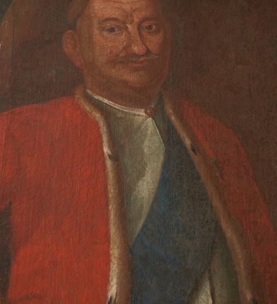 Zdjęcie nr 13: Obraz w kształcie stojącego prostokąta ujętego dekoracyjną ramą z uszakami, motywem paludamentum oraz wyobrażeniem Orderu Orła Białego przedstawia całopostaciową sylwetkę Franciszka Szwracenberg-Czernego. Twarz, zwróconego w trzech czwartych w prawo mężczyzny charakteryzują pozbawione idealizacji cechy portretowe o długim, zaokrąglonym na końcu nosie, lekko podkrążonych oczach, szerokich ustach, spiczastych wąsach, bruzdach na czole oraz wydatnym podbródku. Ubrany jest on w długi, biały żupan przewiązany czerwonym pasem kontuszowym oraz czerwoną, podszytą futrem gronostajowym delię. Przez piersi przewieszona jest błękitna szarfa będąca fragmentem garnituru Orderu Orła Białego. U lewego boku przypięta jest szabla. Prawą rękę wspiera na biodrze, lewą, w której trzyma rysunek fasady kościoła, na niewielkim stoliku o wygiętych nogach. W tle, po lewej stronie kompozycji widoczna jest granatowa, obszyta złotą frędzlą kotara.     