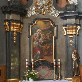 Zdjęcie nr 1: Nastawa ołtarza stiukowa, architektoniczna, jednoosiowa, jednokondygnacyjna, o wklęsłym licu, ze zwieńczeniem oraz osadzona na wysokim cokole. Ołtarz drewniany, sarkofagowy z drewnianą, silnie wysuniętą mensą. Retabulum ujęte parą zdwojonych pilastrów o trzonach dekorowanych konsolkami i kampanulami na froncie, dźwigających przerwane belkowanie. W polu środkowym umieszczono obraz Świętej Rodziny ujęty profilowaną ramą w formie stojącego prostokąta zamkniętego łukiem odcinkowym, nadwieszonym z uskokiem i uszakami po bokach, wklęsłego u spodu. Poniżej obrazu znajduje się płycina ujęta spływami wolutowymi, zamknięta fragmentem gzymsu w formie łuku odcinkowego. W jej polu jest kartusz o fantazyjnym wykroju. Zwieńczenie ujęto parą spływów wolutowych i zamknięto fragmentem wklęsło-wypukłego gzymsu, na którym jest płomienisty wazon. Na końcach spływów wolutowych znajduje się para siedzących putt.  
Pole zwieńczenia wypełniają płaskorzeźbione obłoki z uskrzydlonymi główkami anielskimi oraz ukazana na ich tle promienista gloria z parą główek anielskich pośrodku. Struktura retabulum jest marmoryzowana w kolorze szaro-brązowym i ciemnoszarym, ze złoconymi i srebrzonymi detalami.
