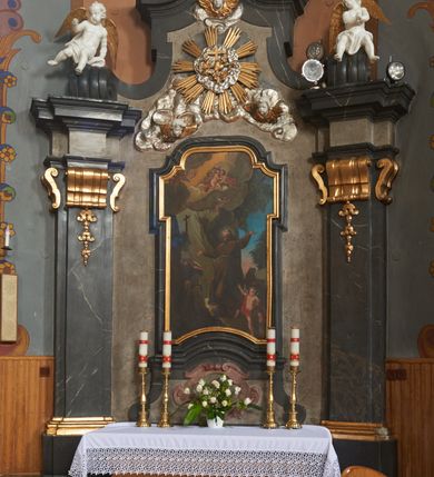 Zdjęcie nr 2: Nastawa ołtarza jest stiukowa, architektoniczna, jednoosiowa, jednokondygnacyjna, o wklęsłym licu, ze zwieńczeniem oraz osadzona na wysokim cokole. Ołtarz jest drewniany, sarkofagowy z drewnianą, silnie wysuniętą, drewnianą mensą. Retabulum ujęte jest parą zdwojonych pilastrów o trzonach dekorowanych konsolkami i kampanulami na froncie, dźwigających przerwane belkowanie. W polu środkowym umieszczono obraz św. Franciszka ujęty profilowaną ramą w formie stojącego prostokąta zamkniętego łukiem odcinkowym, nadwieszonym z uskokiem i uszakami po bokach, wklęsłego u spodu. Poniżej obrazu znajduje się płycina ujęta spływami wolutowymi, zamknięta fragmentem gzymsu w formie łuku odcinkowego. W jej polu jest kartusz o fantazyjnym wykroju. Zwieńczenie ujęto parą spływów wolutowych i zamknięto fragmentem wklęsło-wypukłego gzymsu, na którym jest krzyż na kuli. Na końcach spływów wolutowych znajduje się para siedzących putt.  
Pole zwieńczenia wypełniają płaskorzeźbione obłoki z uskrzydlonymi główkami anielskimi oraz ukazana na ich tle promienista gloria, po środku której znajduje się krzyż, kotwica, serce i wieniec laurowy (symbole Wiary, Nadziei i Miłości). Struktura retabulum jest marmoryzowana w kolorze szaro-brązowym i ciemnoszarym, ze złoconymi i srebrzonymi detalami.