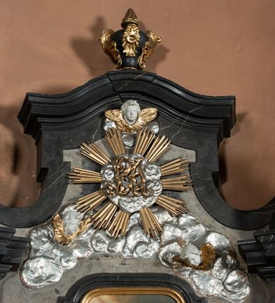 Zdjęcie nr 27: Nastawa ołtarza stiukowa, architektoniczna, jednoosiowa, jednokondygnacyjna, o wklęsłym licu, ze zwieńczeniem oraz osadzona na wysokim cokole. Ołtarz drewniany, sarkofagowy z drewnianą, silnie wysuniętą mensą. Retabulum ujęte jest parą zdwojonych pilastrów o trzonach dekorowanych konsolkami i kampanulami na froncie, dźwigających przerwane belkowanie. W polu środkowym umieszczono obraz św. Mikołaja ujęty profilowaną ramą w formie stojącego prostokąta zamkniętego łukiem odcinkowym, nadwieszonym z uskokiem i uszakami po bokach, wklęsłego u spodu. Poniżej obrazu znajduje się płycina ujęta spływami wolutowymi, zamknięta fragmentem gzymsu w formie łuku odcinkowego. W jej polu jest kartusz o fantazyjnym wykroju. Zwieńczenie ujęto parą spływów wolutowych i zamknięto fragmentem wklęsło-wypukłego gzymsu, na którym jest płomienisty wazon. Na końcach spływów wolutowych znajduje się para siedzących putt.  
Pole zwieńczenia wypełniają płaskorzeźbione obłoki z uskrzydlonymi główkami anielskimi oraz ukazana na ich tle promienista gloria z monogramem maryjnym pośrodku. Struktura retabulum jest marmoryzowana w kolorze szaro-brązowym i ciemnoszarym, ze złoconymi i srebrzonymi detalami.
