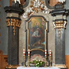 Zdjęcie nr 1: Nastawa ołtarza stiukowa, architektoniczna, jednoosiowa, jednokondygnacyjna, o wklęsłym licu, ze zwieńczeniem oraz osadzona na wysokim cokole. Ołtarz drewniany, sarkofagowy z drewnianą, silnie wysuniętą mensą. Retabulum ujęte parą zdwojonych pilastrów o trzonach dekorowanych konsolkami i kampanulami na froncie, dźwigających przerwane belkowanie. W polu środkowym umieszczono obraz św. Jana Nepomucena ujęty profilowaną ramą w formie stojącego prostokąta zamkniętego łukiem odcinkowym, nadwieszonym z uskokiem i uszakami po bokach, wklęsłego u spodu. Poniżej obrazu znajduje się płycina ujęta spływami wolutowymi, zamknięta fragmentem gzymsu w formie łuku odcinkowego. W jej polu jest kartusz o fantazyjnym wykroju. Zwieńczenie ujęto parą spływów wolutowych i zamknięto fragmentem wklęsło-wypukłego gzymsu, na którym jest krzyż na kuli. Na końcach spływów wolutowych znajduje się para siedzących putt.  
Pole zwieńczenia wypełniają płaskorzeźbione obłoki z uskrzydlonymi główkami anielskimi oraz ukazana na ich tle promienista gloria. Struktura retabulum jest marmoryzowana w kolorze szaro-brązowym i ciemnoszarym, ze złoconymi i srebrzonymi detalami.

