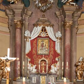 Zdjęcie nr 1: Architektoniczna nastawa ołtarzowa jest jednoosiowa, jednokondygnacyjna ze zwieńczeniem, osadzona na cokole, ujęta parą kolumn o kapitelach kompozytowych, wysuniętych przed strukturę. Każda usytuowana jest na tle pary wklęsłych, ustawionych pod kątem pilastrów, zdwojonych po zewnętrznej stronie nastawy. Kolumny i pilastry wspierają przerwane belkowanie. Pole środkowe retabulum zaaranżowane jest w formie paludamentu pod baldachimem, którego krawędź ozdobiono lambrekinem. Tkanina po bokach jest podwiązana wstęgami. Na tle paludamentu znajduje się niewielka wnęka w kształcie stojącego prostokąta, ujęta profilowaną, dekorowaną ornamentem ramą z wizerunkiem Matki Boskiej z Dzieciątkiem. Ponad obrazem umieszczono płaskorzeźbione oko Opatrzności Bożej ukazane na tle obłoków i glorii promienistej. Zwieńczenie ołtarza ujęte jest parą wolut spływających na belkowanie i zamknięte fragmentem gzymsu w formie łuku odcinkowego zakończonego wolutami. Po bokach znajduje się para adorujących aniołów. W polu zwieńczenia zlokalizowano owalny medalion z monogramem maryjnym, ujęty promienistą glorią oraz otokiem z obłoków i uskrzydlonych główek anielskich. Nastawę flankują cokoły z figurami św. Anny i św. Joachima. Struktura retabulum jest marmoryzowana w kolorze szaro-brązowym i ciemnoróżowym, detale polichromowane na biało, złocone i srebrzone.