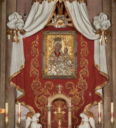 Zdjęcie nr 9: Architektoniczna nastawa ołtarzowa jest jednoosiowa, jednokondygnacyjna ze zwieńczeniem, osadzona na cokole, ujęta parą kolumn o kapitelach kompozytowych, wysuniętych przed strukturę. Każda usytuowana jest na tle pary wklęsłych, ustawionych pod kątem pilastrów, zdwojonych po zewnętrznej stronie nastawy. Kolumny i pilastry wspierają przerwane belkowanie. Pole środkowe retabulum zaaranżowane jest w formie paludamentu pod baldachimem, którego krawędź ozdobiono lambrekinem. Tkanina po bokach jest podwiązana wstęgami. Na tle paludamentu znajduje się niewielka wnęka w kształcie stojącego prostokąta, ujęta profilowaną, dekorowaną ornamentem ramą z wizerunkiem Matki Boskiej z Dzieciątkiem. Ponad obrazem umieszczono płaskorzeźbione oko Opatrzności Bożej ukazane na tle obłoków i glorii promienistej. Zwieńczenie ołtarza ujęte jest parą wolut spływających na belkowanie i zamknięte fragmentem gzymsu w formie łuku odcinkowego zakończonego wolutami. Po bokach znajduje się para adorujących aniołów. W polu zwieńczenia zlokalizowano owalny medalion z monogramem maryjnym, ujęty promienistą glorią oraz otokiem z obłoków i uskrzydlonych główek anielskich. Nastawę flankują cokoły z figurami św. Anny i św. Joachima. Struktura retabulum jest marmoryzowana w kolorze szaro-brązowym i ciemnoróżowym, detale polichromowane na biało, złocone i srebrzone.