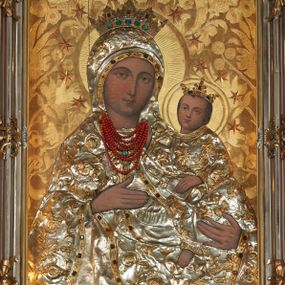 Zdjęcie nr 1: Obraz w kształcie stojącego prostokąta przedstawia Matkę Boską z Dzieciątkiem wyobrażoną w półpostaci. Sylwetka Marii nieznacznie zwrócona jest w lewo. Jej zaokrągloną twarz charakteryzują łagodne, wyraziste rysy o silnie podkreślonych liniach łuków brwiowych i prostego nosa wydobyte światłocieniem. Oczy są duże, usta drobne, a karnacja śniada. Partie szat, łącznie z maforionem zasłaniającym włosy Marii, pokryte są metalowymi, srebrzonymi sukienkami, na powierzchni których odtworzono w ogólnych zarysach przebieg fałdów; szaty zdobione są motywem stylizowanej, ukwieconej, złoconej wici roślinnej, o kameryzowanych lamówkach. Maria prawą ręką o wyprostowanych palcach wskazuje na trzymane na lewej ręce Dzieciątko, w trzech czwartych skierowane w lewo. Zwróconą niemal na wprost twarz charakteryzuje podobny jak w przypadku Marii sposób modelunku, okalają ją krótkie, brązowe włosy. Ubraną w długą tunikę sylwetkę Jezusa także osłania metalowa sukienka. Lewą ręką podtrzymuje on na kolanach księgę, prawą unosi w geście błogosławieństwa; u dołu widoczna jest nieobuta, swobodnie zwisająca stopa Dzieciątka. Postaci ukazane są na tłoczonym w gruncie, złoconym tle dekorowanym motywem roślinnym. Zwieńczone otwartymi, kameryzowanymi koronami głowy okalają nimby i wieńce z gwiazd. Wizerunek ujęty profilowaną, srebrzoną ramą zdobioną złoconymi motywami rocaille.