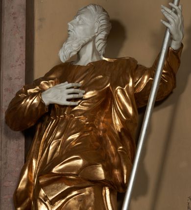 Zdjęcie nr 1: Figura ustawiona na na kwadratowej podstawie, drążona z tyłu, przedstawia stojącego św. Joachima, wyobrażonego w całej postaci. zwróconego nieznacznie w prawo, z uniesioną ku górze głową. Prawa ręka św. Joachima spoczywa na piersi, w lewej, lekko zgiętej w łokciu i odsuniętej w bok trzyma szufle pasterską. Twarz jest pociągła, wychudzona, z długim zarostem i o wyrazistych rysach z silnie uwypuklonymi kośćmi policzkowymi, liniami łuków brwiowych, wąskim nosem, małymi, rozchylonymi, pełnymi ustami z uniesioną górną wargą oraz dużymi, głęboko osadzonymi oczami spoglądającymi w górę. Krótkie, lekko falowane włosy układają się w regularne pukle. Smukłą i wydłużoną sylwetkę świętego osłania przylegająca do ciała, długa, drapowana suknia przepasana w talii oraz narzucony na plecy i opadający wzdłuż boków płaszcz z fragmentem tkaniny zasłaniającym częściowo lewe udo. Kolorystyka odsłoniętych partii ciała utrzymana jest w bieli, szaty złocone, drzewiec, na którym osadzona jest szufla srebrzony.