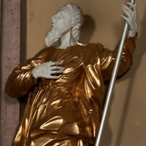 Zdjęcie nr 1: Figura ustawiona na na kwadratowej podstawie, drążona z tyłu, przedstawia stojącego św. Joachima, wyobrażonego w całej postaci. zwróconego nieznacznie w prawo, z uniesioną ku górze głową. Prawa ręka św. Joachima spoczywa na piersi, w lewej, lekko zgiętej w łokciu i odsuniętej w bok trzyma szufle pasterską. Twarz jest pociągła, wychudzona, z długim zarostem i o wyrazistych rysach z silnie uwypuklonymi kośćmi policzkowymi, liniami łuków brwiowych, wąskim nosem, małymi, rozchylonymi, pełnymi ustami z uniesioną górną wargą oraz dużymi, głęboko osadzonymi oczami spoglądającymi w górę. Krótkie, lekko falowane włosy układają się w regularne pukle. Smukłą i wydłużoną sylwetkę świętego osłania przylegająca do ciała, długa, drapowana suknia przepasana w talii oraz narzucony na plecy i opadający wzdłuż boków płaszcz z fragmentem tkaniny zasłaniającym częściowo lewe udo. Kolorystyka odsłoniętych partii ciała utrzymana jest w bieli, szaty złocone, drzewiec, na którym osadzona jest szufla srebrzony.