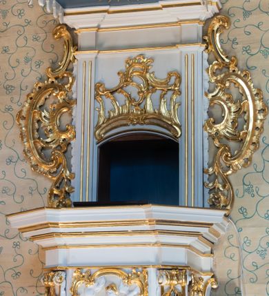 Zdjęcie nr 1: Ambona, przyścienna, wisząca, z jednobiegowymi schodami od strony prezbiterium. Kosz w formie czworoboku o ściętych narożach ze spływami wolutowymi. Ścianki kosza zdobione są nieregularną ramą z ornamentu rocaille&#039;owego. W płycinie czołowej (południowej) płaskorzeźba Siewcy. Woluty zdobione ornamentami kwiatowymi w formie girland podtrzymują mocno wysunięte, wyłamane na ich osi belkowanie. Kosz od dołu zakończony jest stożkiem ujętym czterema wolutami, dekorowanymi motywami roślinnymi, zakończony roacille’ową szyszką. Zaplecek w kształcie stojącego prostokąta, ujęty dwoma kanelowanymi pilastrami podtrzymującymi belkowanie wyłamane nad osią główną. W dolnej części zaplecka drzwiczki zamknięte łukiem odcinkowym, a w górnej płaskorzeźbiona dekoracja rocaille’owa. Po bokach zaplecka ażurowe rocaille’owe uszy. Baldachim powtarzający rzut kosza z lambrekinem podwieszonym u dołu i zamknięty silnie wysuniętym gzymsem. Zwieńczenie uformowane z czterech wolut spiętych w kabłąk, na którego szczycie na niskim kwadratowym cokole ustawiona jest figura Michała Archanioła depczącego szatana. W podniebieniu gołębica Ducha Świętego na tle promienistej glorii. Polichromia w kolorze białym, ornamentyka złocona, gołębica srebrzona, podniebienie baldachimu malowane na niebiesko.
