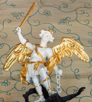 Zdjęcie nr 5: Ambona, przyścienna, wisząca, z jednobiegowymi schodami od strony prezbiterium. Kosz w formie czworoboku o ściętych narożach ze spływami wolutowymi. Ścianki kosza zdobione są nieregularną ramą z ornamentu rocaille'owego. W płycinie czołowej (południowej) płaskorzeźba Siewcy. Woluty zdobione ornamentami kwiatowymi w formie girland podtrzymują mocno wysunięte, wyłamane na ich osi belkowanie. Kosz od dołu zakończony jest stożkiem ujętym czterema wolutami, dekorowanymi motywami roślinnymi, zakończony roacille’ową szyszką. Zaplecek w kształcie stojącego prostokąta, ujęty dwoma kanelowanymi pilastrami podtrzymującymi belkowanie wyłamane nad osią główną. W dolnej części zaplecka drzwiczki zamknięte łukiem odcinkowym, a w górnej płaskorzeźbiona dekoracja rocaille’owa. Po bokach zaplecka ażurowe rocaille’owe uszy. Baldachim powtarzający rzut kosza z lambrekinem podwieszonym u dołu i zamknięty silnie wysuniętym gzymsem. Zwieńczenie uformowane z czterech wolut spiętych w kabłąk, na którego szczycie na niskim kwadratowym cokole ustawiona jest figura Michała Archanioła depczącego szatana. W podniebieniu gołębica Ducha Świętego na tle promienistej glorii. Polichromia w kolorze białym, ornamentyka złocona, gołębica srebrzona, podniebienie baldachimu malowane na niebiesko.
