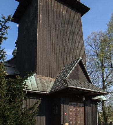Zdjęcie nr 44: Kościół drewniany, orientowany, jednonawowy o konstrukcji zrębowej, oszalowany. Prezbiterium kwadratowe o wielobocznym zamknięciu z zakrystią od północy. Nawa szersza, prawie kwadratowa, przy niej od północy kaplica i składzik później dostawiony; od południa i od zachodu kruchty. Korpus nakryty dachem dwuspadowym, jednokalenicowym, z barokową wieżyczką na sygnaturkę na kalenicy; składzik nakryty dachem pulpitowym. Wewnątrz stropy kasetonowe. Otwór tęczy o profilowanym łuku półkolistym podwyższonym; belka profilowana, na niej grupa Ukrzyżowania. Chór muzyczny wsparty na dwóch słupach. Kaplica otwarta do nawy półkolistą arkadą. Troje drzwi o ozdobnych obramieniach uszatych, schodkowatych i uszato-schodkowatych, ze starymi okuciami. Wieża nowa, izbicowa o pochyłych ścianach, zwieńczona ostrosłupowym hełmem.
