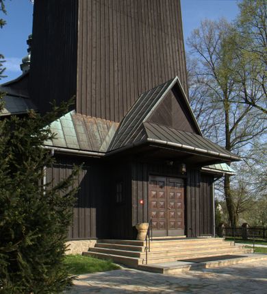 Zdjęcie nr 41: Kościół drewniany, orientowany, jednonawowy o konstrukcji zrębowej, oszalowany. Prezbiterium kwadratowe o wielobocznym zamknięciu z zakrystią od północy. Nawa szersza, prawie kwadratowa, przy niej od północy kaplica i składzik później dostawiony; od południa i od zachodu kruchty. Korpus nakryty dachem dwuspadowym, jednokalenicowym, z barokową wieżyczką na sygnaturkę na kalenicy; składzik nakryty dachem pulpitowym. Wewnątrz stropy kasetonowe. Otwór tęczy o profilowanym łuku półkolistym podwyższonym; belka profilowana, na niej grupa Ukrzyżowania. Chór muzyczny wsparty na dwóch słupach. Kaplica otwarta do nawy półkolistą arkadą. Troje drzwi o ozdobnych obramieniach uszatych, schodkowatych i uszato-schodkowatych, ze starymi okuciami. Wieża nowa, izbicowa o pochyłych ścianach, zwieńczona ostrosłupowym hełmem.
