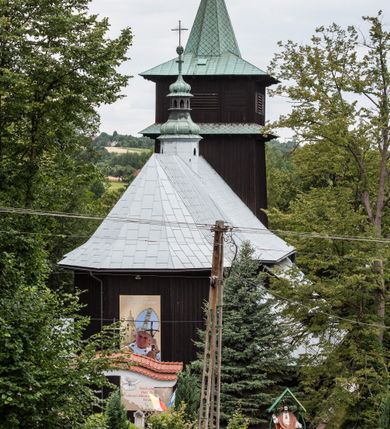 Zdjęcie nr 20: Kościół drewniany, orientowany, jednonawowy o konstrukcji zrębowej, oszalowany. Prezbiterium kwadratowe o wielobocznym zamknięciu z zakrystią od północy. Nawa szersza, prawie kwadratowa, przy niej od północy kaplica i składzik później dostawiony; od południa i od zachodu kruchty. Korpus nakryty dachem dwuspadowym, jednokalenicowym, z barokową wieżyczką na sygnaturkę na kalenicy; składzik nakryty dachem pulpitowym. Wewnątrz stropy kasetonowe. Otwór tęczy o profilowanym łuku półkolistym podwyższonym; belka profilowana, na niej grupa Ukrzyżowania. Chór muzyczny wsparty na dwóch słupach. Kaplica otwarta do nawy półkolistą arkadą. Troje drzwi o ozdobnych obramieniach uszatych, schodkowatych i uszato-schodkowatych, ze starymi okuciami. Wieża nowa, izbicowa o pochyłych ścianach, zwieńczona ostrosłupowym hełmem.
