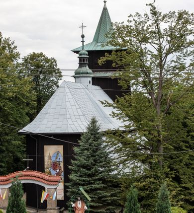 Zdjęcie nr 19: Kościół drewniany, orientowany, jednonawowy o konstrukcji zrębowej, oszalowany. Prezbiterium kwadratowe o wielobocznym zamknięciu z zakrystią od północy. Nawa szersza, prawie kwadratowa, przy niej od północy kaplica i składzik później dostawiony; od południa i od zachodu kruchty. Korpus nakryty dachem dwuspadowym, jednokalenicowym, z barokową wieżyczką na sygnaturkę na kalenicy; składzik nakryty dachem pulpitowym. Wewnątrz stropy kasetonowe. Otwór tęczy o profilowanym łuku półkolistym podwyższonym; belka profilowana, na niej grupa Ukrzyżowania. Chór muzyczny wsparty na dwóch słupach. Kaplica otwarta do nawy półkolistą arkadą. Troje drzwi o ozdobnych obramieniach uszatych, schodkowatych i uszato-schodkowatych, ze starymi okuciami. Wieża nowa, izbicowa o pochyłych ścianach, zwieńczona ostrosłupowym hełmem.
