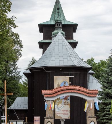 Zdjęcie nr 18: Kościół drewniany, orientowany, jednonawowy o konstrukcji zrębowej, oszalowany. Prezbiterium kwadratowe o wielobocznym zamknięciu z zakrystią od północy. Nawa szersza, prawie kwadratowa, przy niej od północy kaplica i składzik później dostawiony; od południa i od zachodu kruchty. Korpus nakryty dachem dwuspadowym, jednokalenicowym, z barokową wieżyczką na sygnaturkę na kalenicy; składzik nakryty dachem pulpitowym. Wewnątrz stropy kasetonowe. Otwór tęczy o profilowanym łuku półkolistym podwyższonym; belka profilowana, na niej grupa Ukrzyżowania. Chór muzyczny wsparty na dwóch słupach. Kaplica otwarta do nawy półkolistą arkadą. Troje drzwi o ozdobnych obramieniach uszatych, schodkowatych i uszato-schodkowatych, ze starymi okuciami. Wieża nowa, izbicowa o pochyłych ścianach, zwieńczona ostrosłupowym hełmem.
