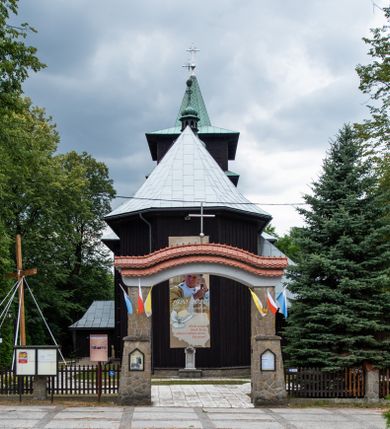 Zdjęcie nr 15: Kościół drewniany, orientowany, jednonawowy o konstrukcji zrębowej, oszalowany. Prezbiterium kwadratowe o wielobocznym zamknięciu z zakrystią od północy. Nawa szersza, prawie kwadratowa, przy niej od północy kaplica i składzik później dostawiony; od południa i od zachodu kruchty. Korpus nakryty dachem dwuspadowym, jednokalenicowym, z barokową wieżyczką na sygnaturkę na kalenicy; składzik nakryty dachem pulpitowym. Wewnątrz stropy kasetonowe. Otwór tęczy o profilowanym łuku półkolistym podwyższonym; belka profilowana, na niej grupa Ukrzyżowania. Chór muzyczny wsparty na dwóch słupach. Kaplica otwarta do nawy półkolistą arkadą. Troje drzwi o ozdobnych obramieniach uszatych, schodkowatych i uszato-schodkowatych, ze starymi okuciami. Wieża nowa, izbicowa o pochyłych ścianach, zwieńczona ostrosłupowym hełmem.
