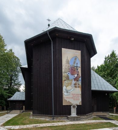 Zdjęcie nr 12: Kościół drewniany, orientowany, jednonawowy o konstrukcji zrębowej, oszalowany. Prezbiterium kwadratowe o wielobocznym zamknięciu z zakrystią od północy. Nawa szersza, prawie kwadratowa, przy niej od północy kaplica i składzik później dostawiony; od południa i od zachodu kruchty. Korpus nakryty dachem dwuspadowym, jednokalenicowym, z barokową wieżyczką na sygnaturkę na kalenicy; składzik nakryty dachem pulpitowym. Wewnątrz stropy kasetonowe. Otwór tęczy o profilowanym łuku półkolistym podwyższonym; belka profilowana, na niej grupa Ukrzyżowania. Chór muzyczny wsparty na dwóch słupach. Kaplica otwarta do nawy półkolistą arkadą. Troje drzwi o ozdobnych obramieniach uszatych, schodkowatych i uszato-schodkowatych, ze starymi okuciami. Wieża nowa, izbicowa o pochyłych ścianach, zwieńczona ostrosłupowym hełmem.
