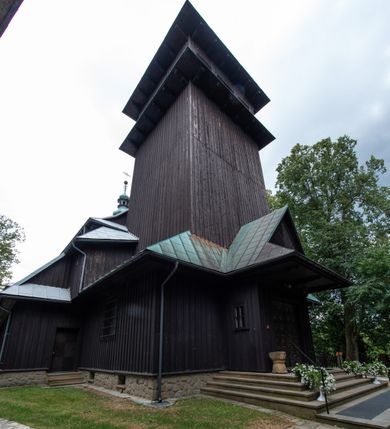 Zdjęcie nr 13: Kościół drewniany, orientowany, jednonawowy o konstrukcji zrębowej, oszalowany. Prezbiterium kwadratowe o wielobocznym zamknięciu z zakrystią od północy. Nawa szersza, prawie kwadratowa, przy niej od północy kaplica i składzik później dostawiony; od południa i od zachodu kruchty. Korpus nakryty dachem dwuspadowym, jednokalenicowym, z barokową wieżyczką na sygnaturkę na kalenicy; składzik nakryty dachem pulpitowym. Wewnątrz stropy kasetonowe. Otwór tęczy o profilowanym łuku półkolistym podwyższonym; belka profilowana, na niej grupa Ukrzyżowania. Chór muzyczny wsparty na dwóch słupach. Kaplica otwarta do nawy półkolistą arkadą. Troje drzwi o ozdobnych obramieniach uszatych, schodkowatych i uszato-schodkowatych, ze starymi okuciami. Wieża nowa, izbicowa o pochyłych ścianach, zwieńczona ostrosłupowym hełmem.
