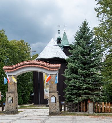 Zdjęcie nr 17: Kościół drewniany, orientowany, jednonawowy o konstrukcji zrębowej, oszalowany. Prezbiterium kwadratowe o wielobocznym zamknięciu z zakrystią od północy. Nawa szersza, prawie kwadratowa, przy niej od północy kaplica i składzik później dostawiony; od południa i od zachodu kruchty. Korpus nakryty dachem dwuspadowym, jednokalenicowym, z barokową wieżyczką na sygnaturkę na kalenicy; składzik nakryty dachem pulpitowym. Wewnątrz stropy kasetonowe. Otwór tęczy o profilowanym łuku półkolistym podwyższonym; belka profilowana, na niej grupa Ukrzyżowania. Chór muzyczny wsparty na dwóch słupach. Kaplica otwarta do nawy półkolistą arkadą. Troje drzwi o ozdobnych obramieniach uszatych, schodkowatych i uszato-schodkowatych, ze starymi okuciami. Wieża nowa, izbicowa o pochyłych ścianach, zwieńczona ostrosłupowym hełmem.
