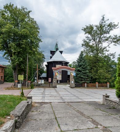 Zdjęcie nr 14: Kościół drewniany, orientowany, jednonawowy o konstrukcji zrębowej, oszalowany. Prezbiterium kwadratowe o wielobocznym zamknięciu z zakrystią od północy. Nawa szersza, prawie kwadratowa, przy niej od północy kaplica i składzik później dostawiony; od południa i od zachodu kruchty. Korpus nakryty dachem dwuspadowym, jednokalenicowym, z barokową wieżyczką na sygnaturkę na kalenicy; składzik nakryty dachem pulpitowym. Wewnątrz stropy kasetonowe. Otwór tęczy o profilowanym łuku półkolistym podwyższonym; belka profilowana, na niej grupa Ukrzyżowania. Chór muzyczny wsparty na dwóch słupach. Kaplica otwarta do nawy półkolistą arkadą. Troje drzwi o ozdobnych obramieniach uszatych, schodkowatych i uszato-schodkowatych, ze starymi okuciami. Wieża nowa, izbicowa o pochyłych ścianach, zwieńczona ostrosłupowym hełmem.
