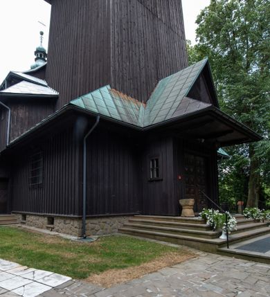 Zdjęcie nr 35: Kościół drewniany, orientowany, jednonawowy o konstrukcji zrębowej, oszalowany. Prezbiterium kwadratowe o wielobocznym zamknięciu z zakrystią od północy. Nawa szersza, prawie kwadratowa, przy niej od północy kaplica i składzik później dostawiony; od południa i od zachodu kruchty. Korpus nakryty dachem dwuspadowym, jednokalenicowym, z barokową wieżyczką na sygnaturkę na kalenicy; składzik nakryty dachem pulpitowym. Wewnątrz stropy kasetonowe. Otwór tęczy o profilowanym łuku półkolistym podwyższonym; belka profilowana, na niej grupa Ukrzyżowania. Chór muzyczny wsparty na dwóch słupach. Kaplica otwarta do nawy półkolistą arkadą. Troje drzwi o ozdobnych obramieniach uszatych, schodkowatych i uszato-schodkowatych, ze starymi okuciami. Wieża nowa, izbicowa o pochyłych ścianach, zwieńczona ostrosłupowym hełmem.
