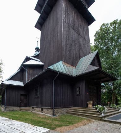 Zdjęcie nr 24: Kościół drewniany, orientowany, jednonawowy o konstrukcji zrębowej, oszalowany. Prezbiterium kwadratowe o wielobocznym zamknięciu z zakrystią od północy. Nawa szersza, prawie kwadratowa, przy niej od północy kaplica i składzik później dostawiony; od południa i od zachodu kruchty. Korpus nakryty dachem dwuspadowym, jednokalenicowym, z barokową wieżyczką na sygnaturkę na kalenicy; składzik nakryty dachem pulpitowym. Wewnątrz stropy kasetonowe. Otwór tęczy o profilowanym łuku półkolistym podwyższonym; belka profilowana, na niej grupa Ukrzyżowania. Chór muzyczny wsparty na dwóch słupach. Kaplica otwarta do nawy półkolistą arkadą. Troje drzwi o ozdobnych obramieniach uszatych, schodkowatych i uszato-schodkowatych, ze starymi okuciami. Wieża nowa, izbicowa o pochyłych ścianach, zwieńczona ostrosłupowym hełmem.
