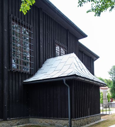 Zdjęcie nr 5: Kościół drewniany, orientowany, jednonawowy o konstrukcji zrębowej, oszalowany. Prezbiterium kwadratowe o wielobocznym zamknięciu z zakrystią od północy. Nawa szersza, prawie kwadratowa, przy niej od północy kaplica i składzik później dostawiony; od południa i od zachodu kruchty. Korpus nakryty dachem dwuspadowym, jednokalenicowym, z barokową wieżyczką na sygnaturkę na kalenicy; składzik nakryty dachem pulpitowym. Wewnątrz stropy kasetonowe. Otwór tęczy o profilowanym łuku półkolistym podwyższonym; belka profilowana, na niej grupa Ukrzyżowania. Chór muzyczny wsparty na dwóch słupach. Kaplica otwarta do nawy półkolistą arkadą. Troje drzwi o ozdobnych obramieniach uszatych, schodkowatych i uszato-schodkowatych, ze starymi okuciami. Wieża nowa, izbicowa o pochyłych ścianach, zwieńczona ostrosłupowym hełmem.
