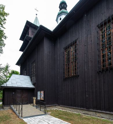 Zdjęcie nr 8: Kościół drewniany, orientowany, jednonawowy o konstrukcji zrębowej, oszalowany. Prezbiterium kwadratowe o wielobocznym zamknięciu z zakrystią od północy. Nawa szersza, prawie kwadratowa, przy niej od północy kaplica i składzik później dostawiony; od południa i od zachodu kruchty. Korpus nakryty dachem dwuspadowym, jednokalenicowym, z barokową wieżyczką na sygnaturkę na kalenicy; składzik nakryty dachem pulpitowym. Wewnątrz stropy kasetonowe. Otwór tęczy o profilowanym łuku półkolistym podwyższonym; belka profilowana, na niej grupa Ukrzyżowania. Chór muzyczny wsparty na dwóch słupach. Kaplica otwarta do nawy półkolistą arkadą. Troje drzwi o ozdobnych obramieniach uszatych, schodkowatych i uszato-schodkowatych, ze starymi okuciami. Wieża nowa, izbicowa o pochyłych ścianach, zwieńczona ostrosłupowym hełmem.
