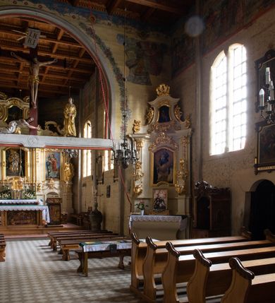 Zdjęcie nr 32: Kościół drewniany, orientowany, jednonawowy o konstrukcji zrębowej, oszalowany. Prezbiterium kwadratowe o wielobocznym zamknięciu z zakrystią od północy. Nawa szersza, prawie kwadratowa, przy niej od północy kaplica i składzik później dostawiony; od południa i od zachodu kruchty. Korpus nakryty dachem dwuspadowym, jednokalenicowym, z barokową wieżyczką na sygnaturkę na kalenicy; składzik nakryty dachem pulpitowym. Wewnątrz stropy kasetonowe. Otwór tęczy o profilowanym łuku półkolistym podwyższonym; belka profilowana, na niej grupa Ukrzyżowania. Chór muzyczny wsparty na dwóch słupach. Kaplica otwarta do nawy półkolistą arkadą. Troje drzwi o ozdobnych obramieniach uszatych, schodkowatych i uszato-schodkowatych, ze starymi okuciami. Wieża nowa, izbicowa o pochyłych ścianach, zwieńczona ostrosłupowym hełmem.
